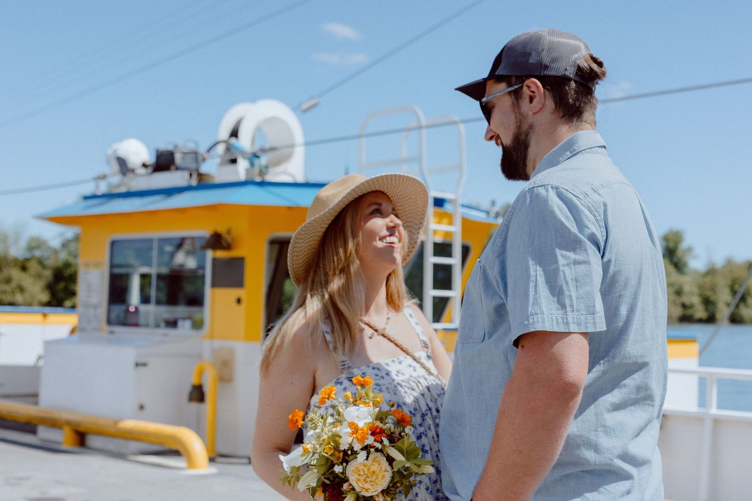 A couple shares a happy moment together on a boat deck with a yellow cabin and sunny sky in the background.