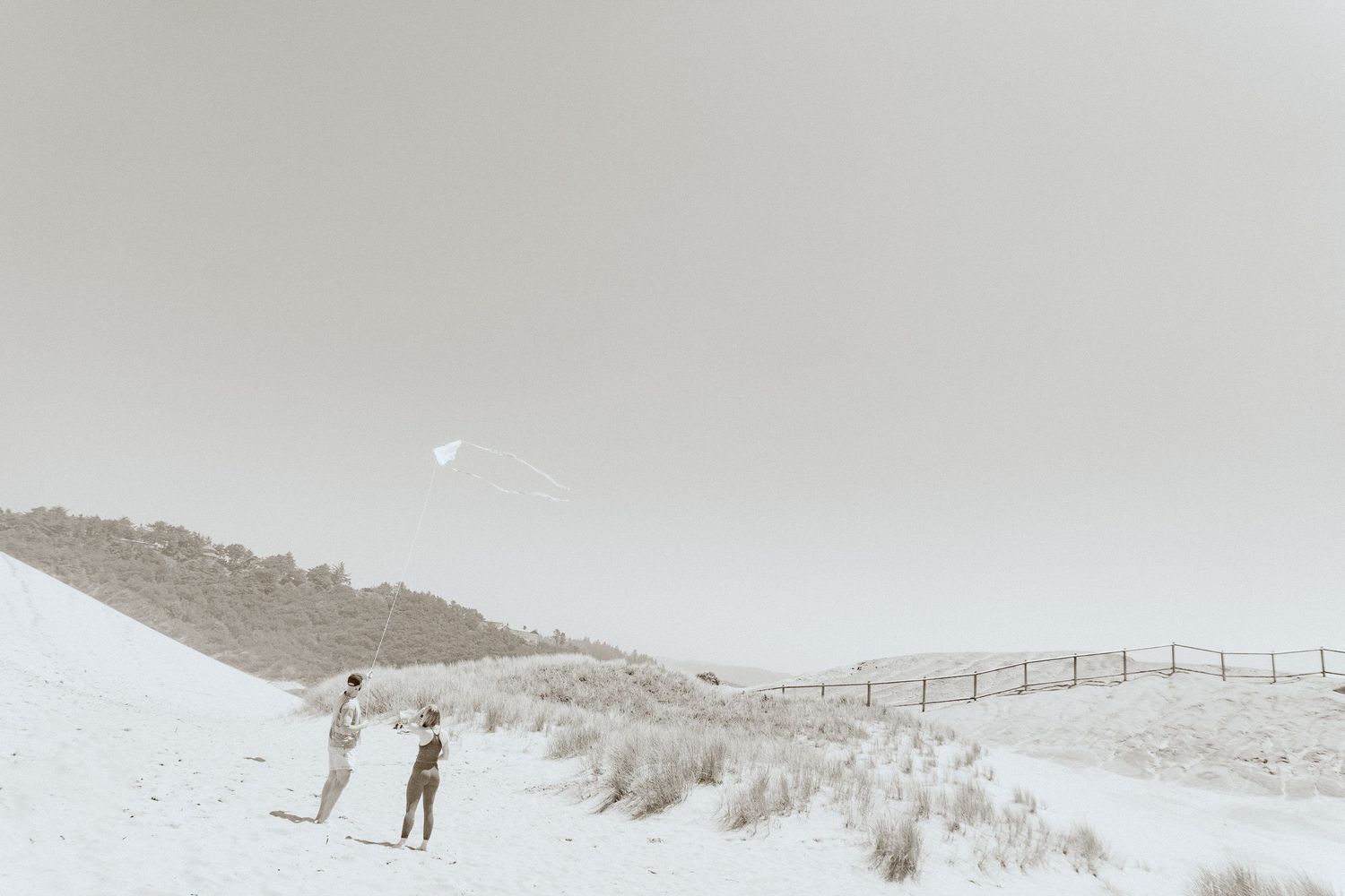 A far away shot of two people flying a kite on a sand dune overlooking the Oregon coast.