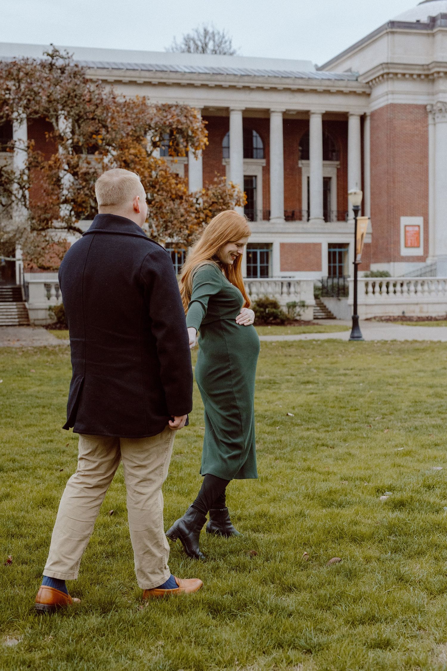 Two people walking on a grassy lawn in front of a stately neoclassical building with columns.
