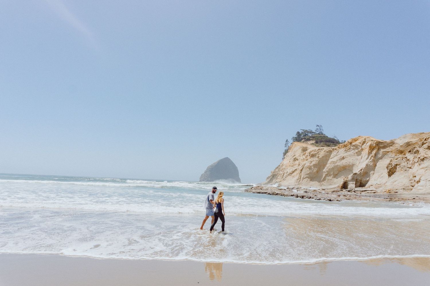 People run along the shore at Pacific Coast in Oregon with waves crashing near dramatic cliffs and rock formations.