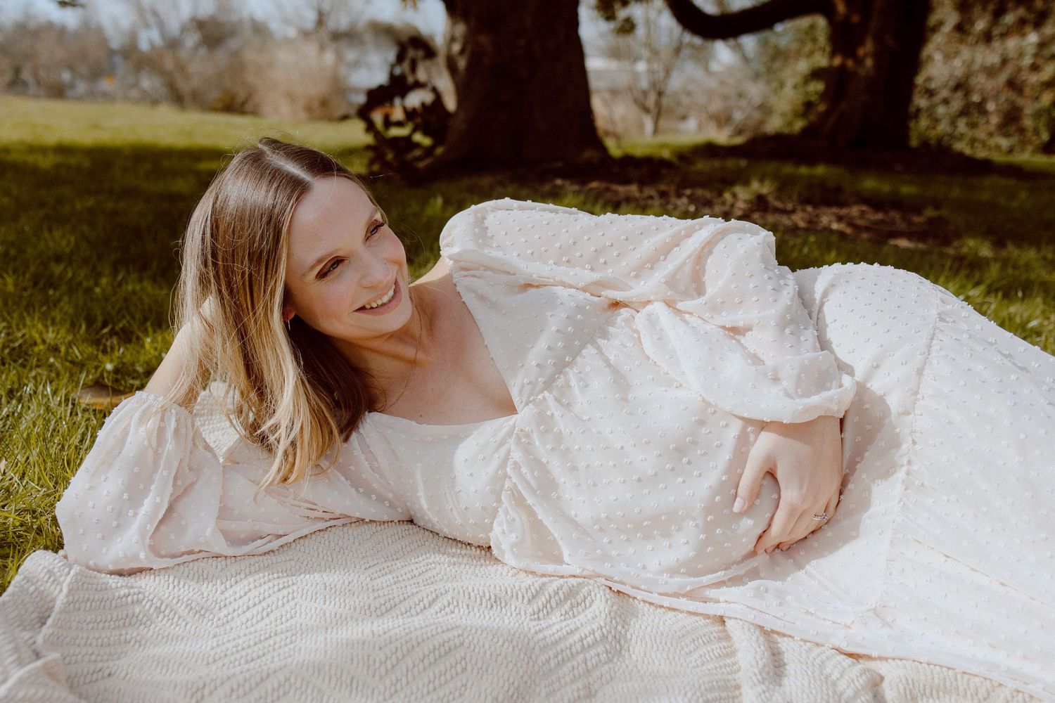 A detailed view of a pregnant mother in delicate white lace and tulle fabric in an outdoor garden setting.