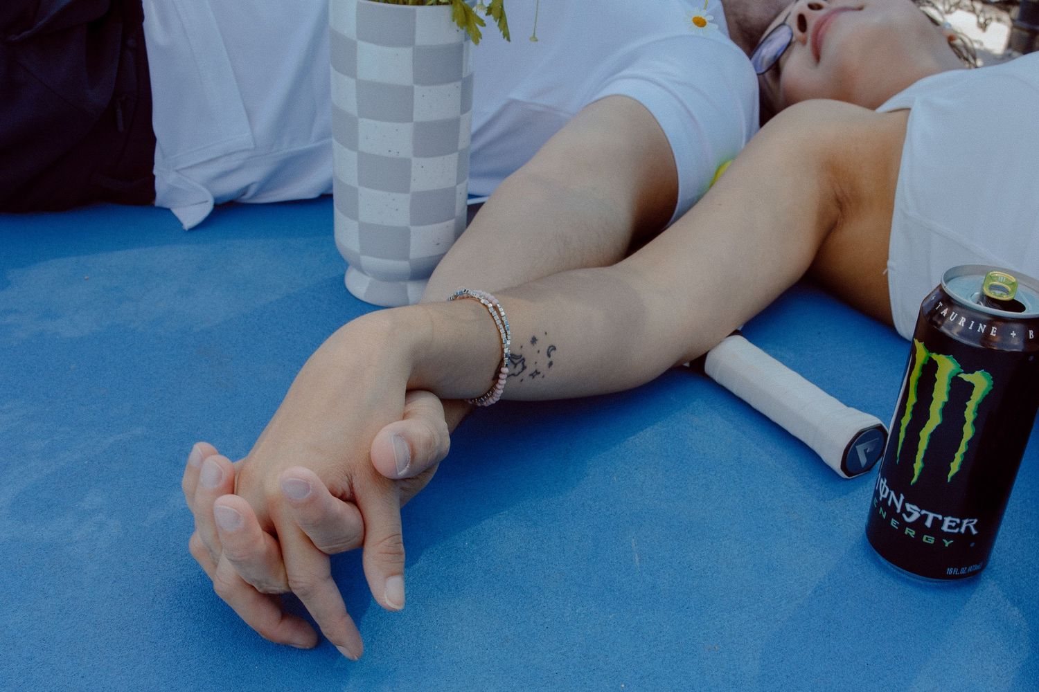 A close up of a couple holding hands while laying down on a tennis court with colorful yellow flowers in the background