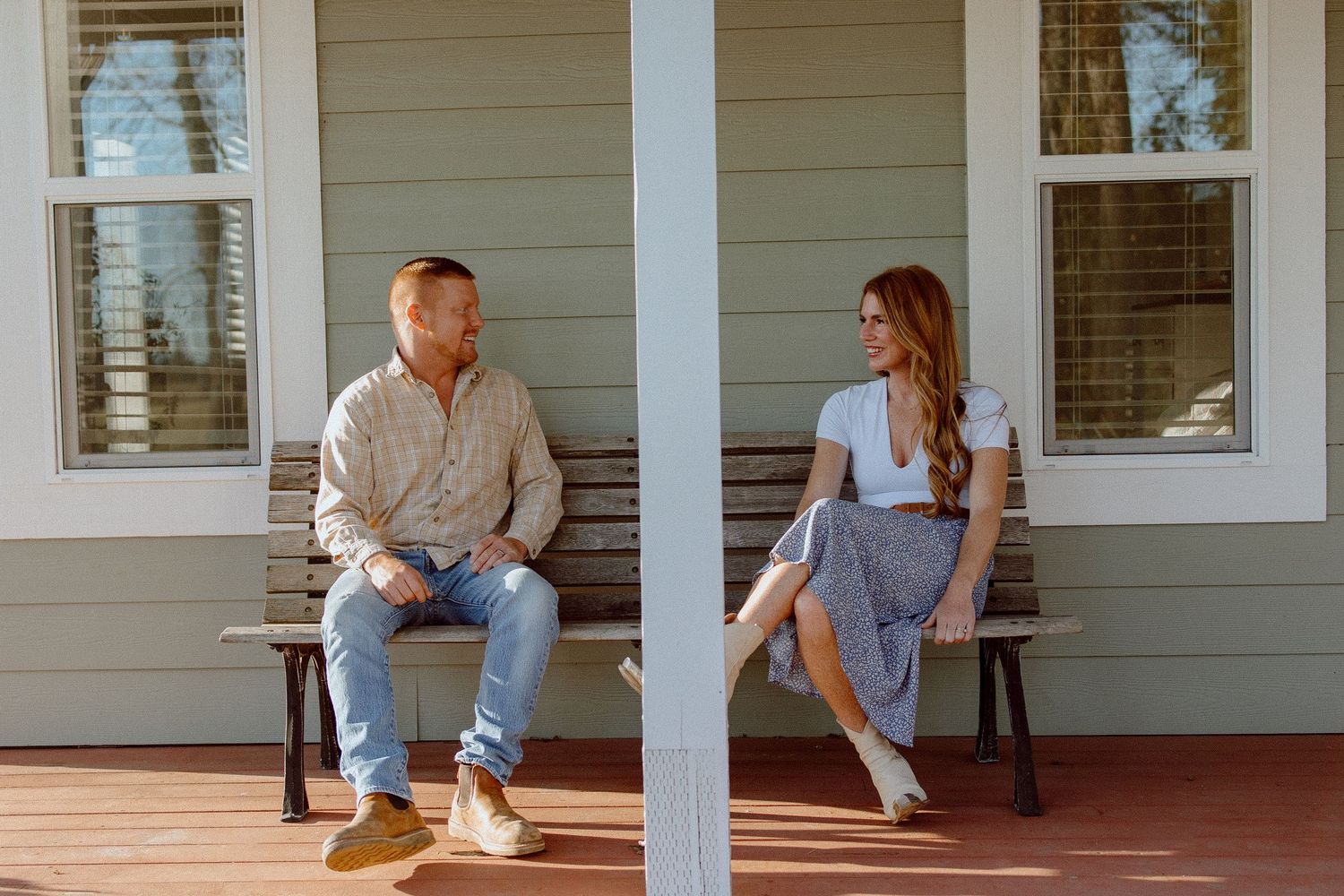 A couple sits together on a farmhouse style porch with white columns and light gray siding.