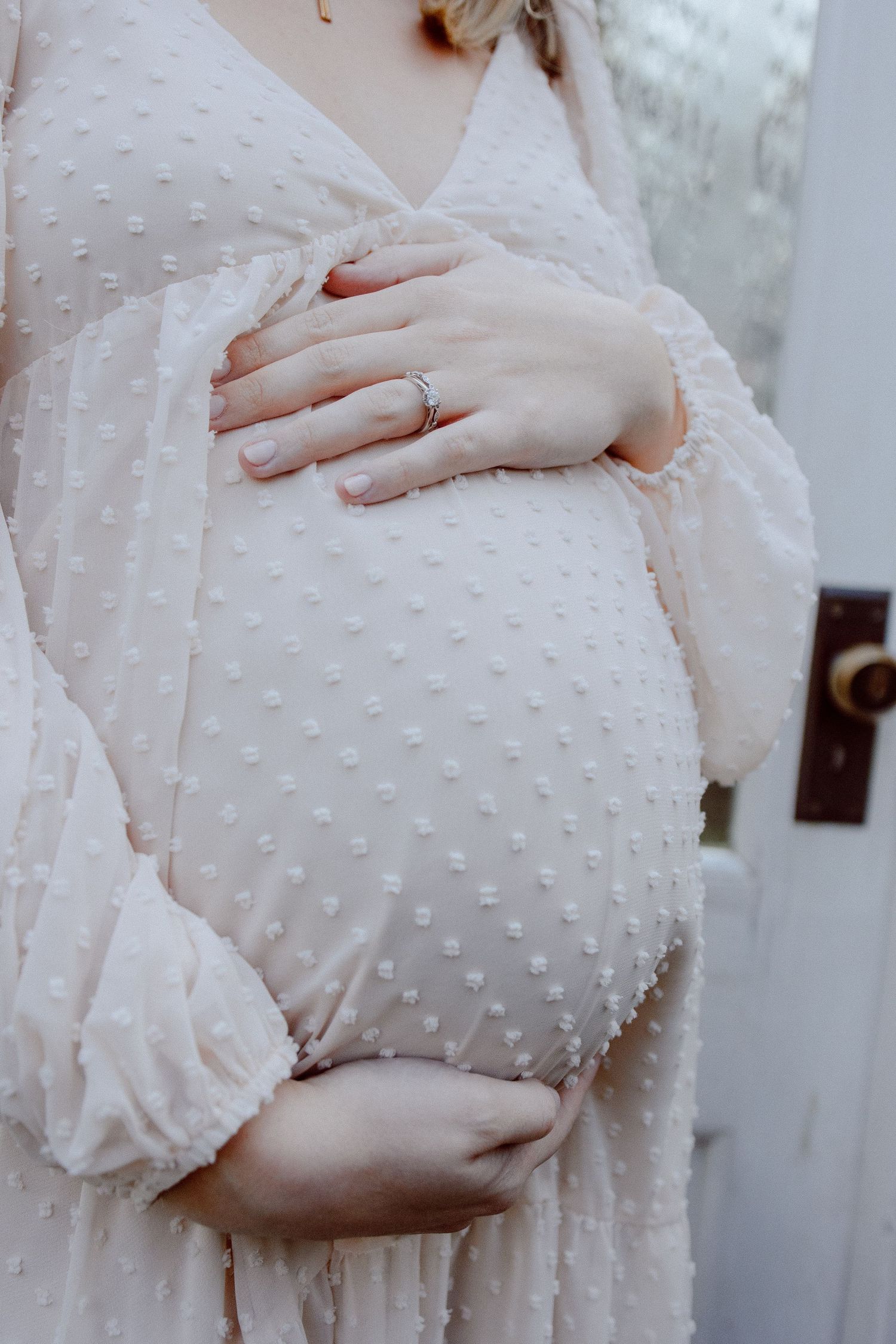 Close-up details of a textured pale dress with small dot embellishments shows hands gently touching her belly.