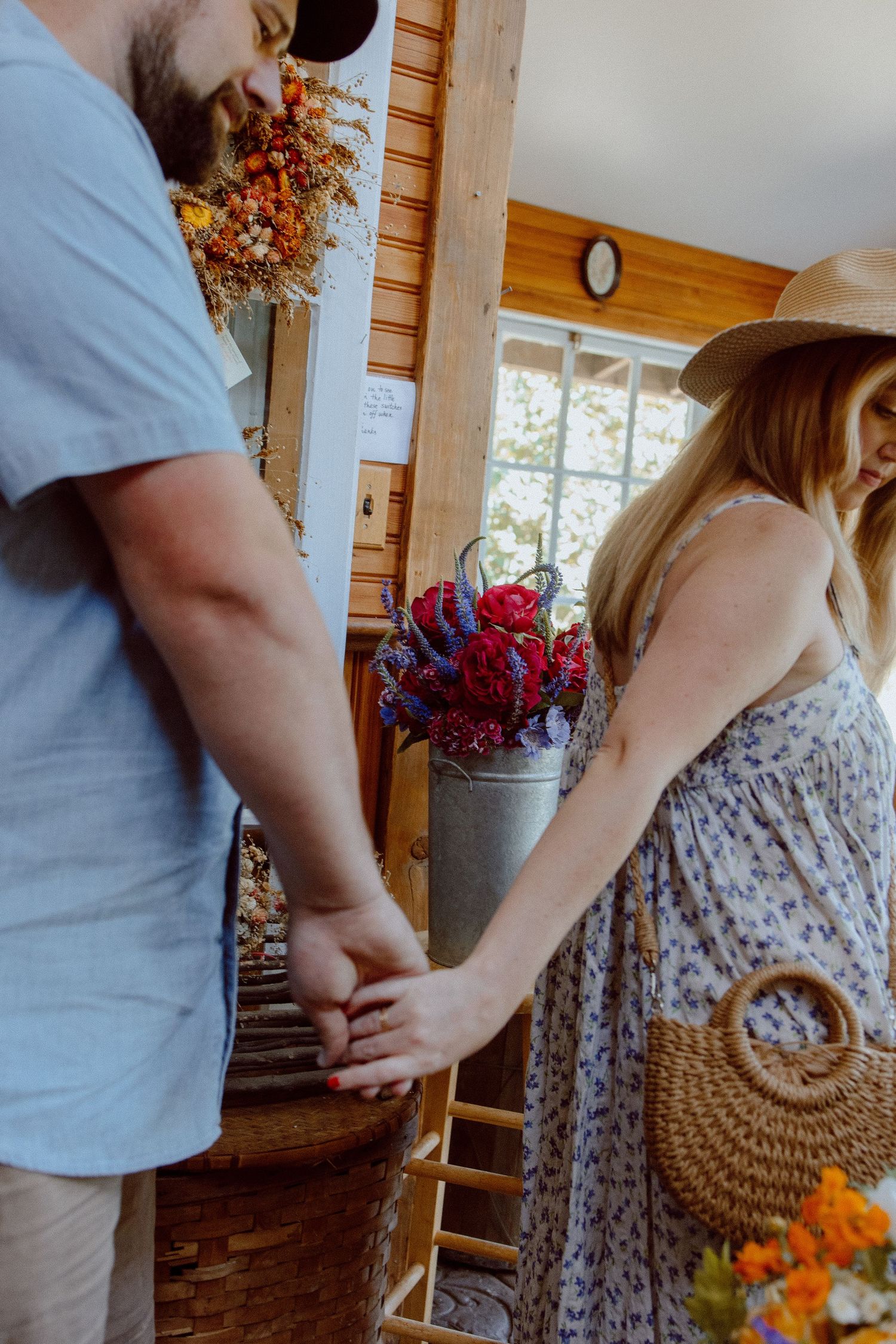 A couple holding hands while walking through a rustic indoor space decorated with dried floral arrangements.