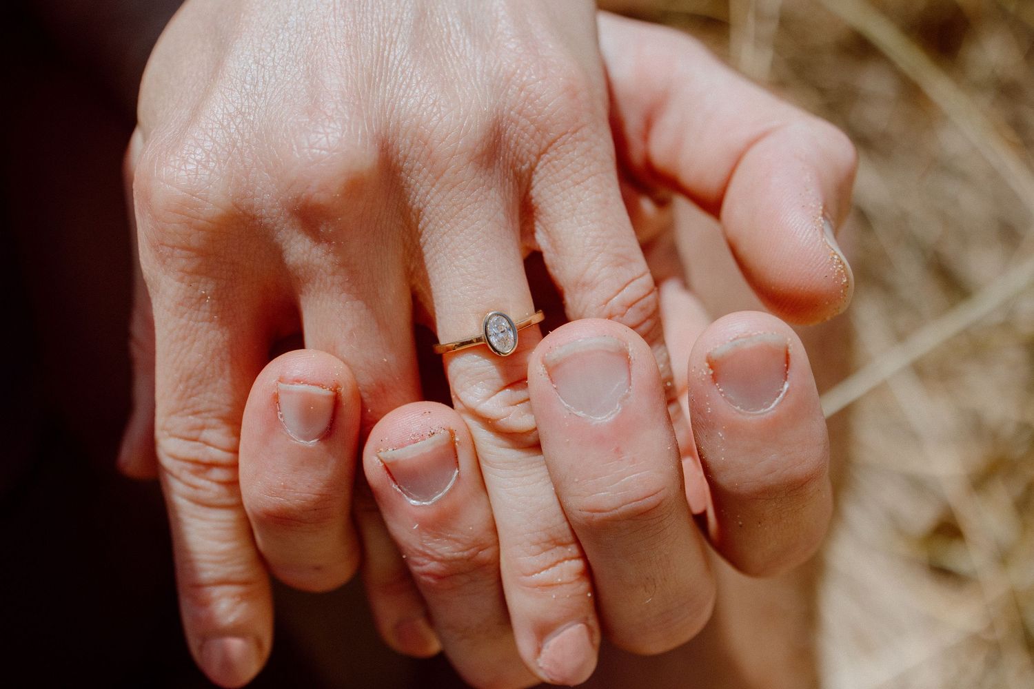 A close-up shot of two hands holding each other with a diamond engagement ring visible.