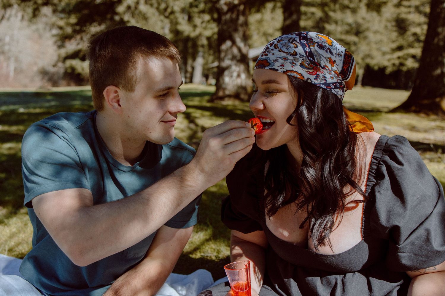 A romantic couple shares an intimate moment in a sunlit outdoor setting, their faces coming close together in tender interaction.