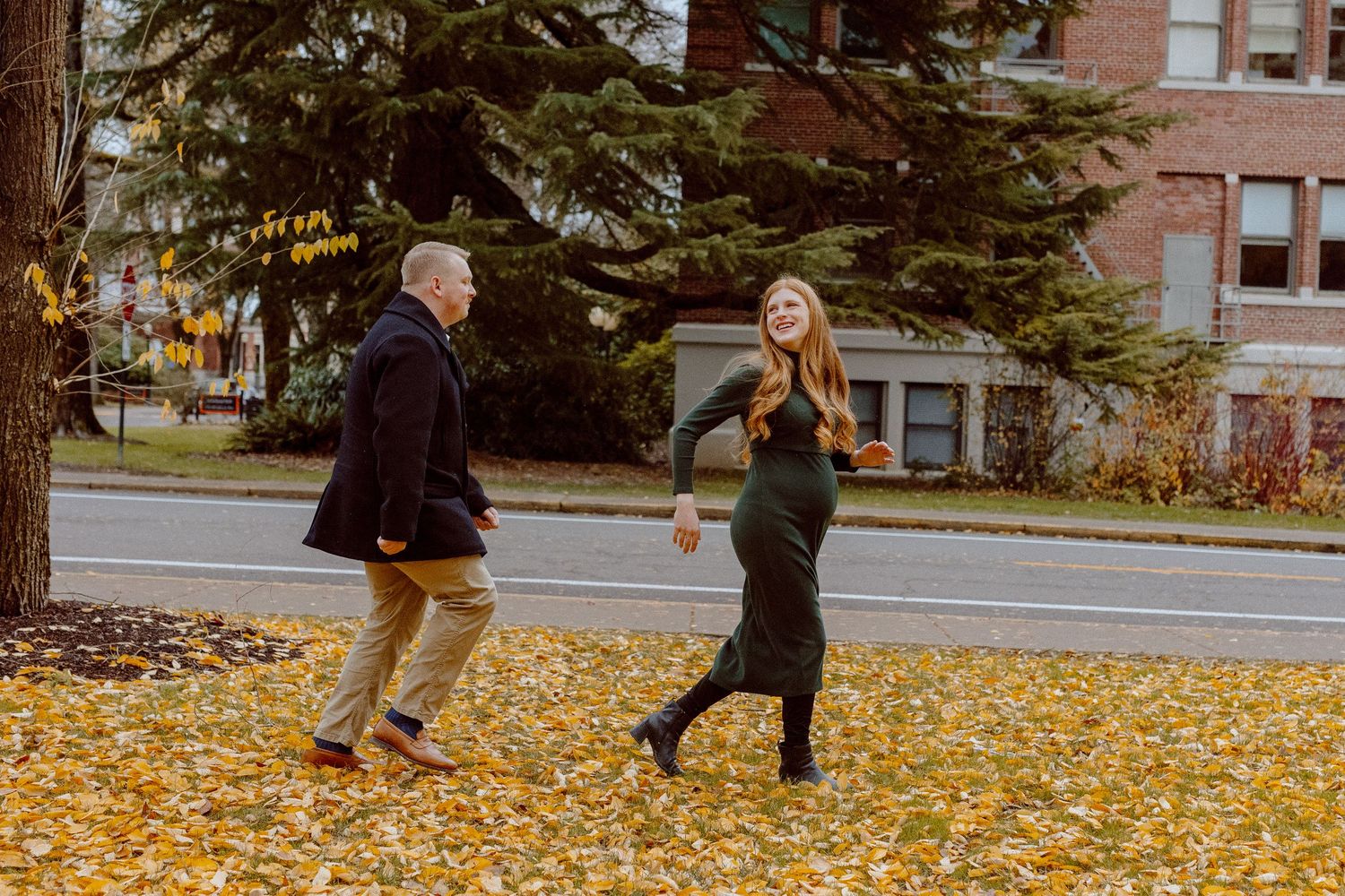 People run through vibrant yellow autumn leaves scattered on a sidewalk near brick buildings.