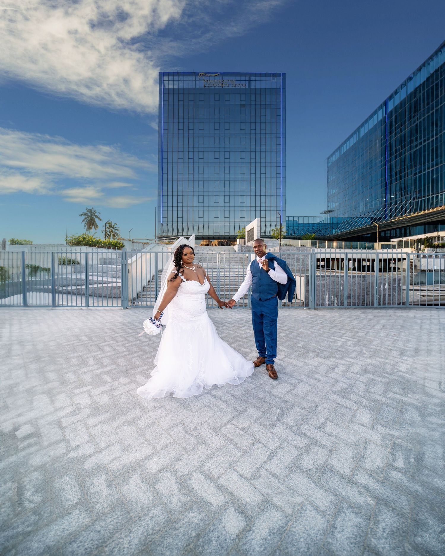 A wedding couple poses on a modern rooftop terrace with glass buildings in the background.