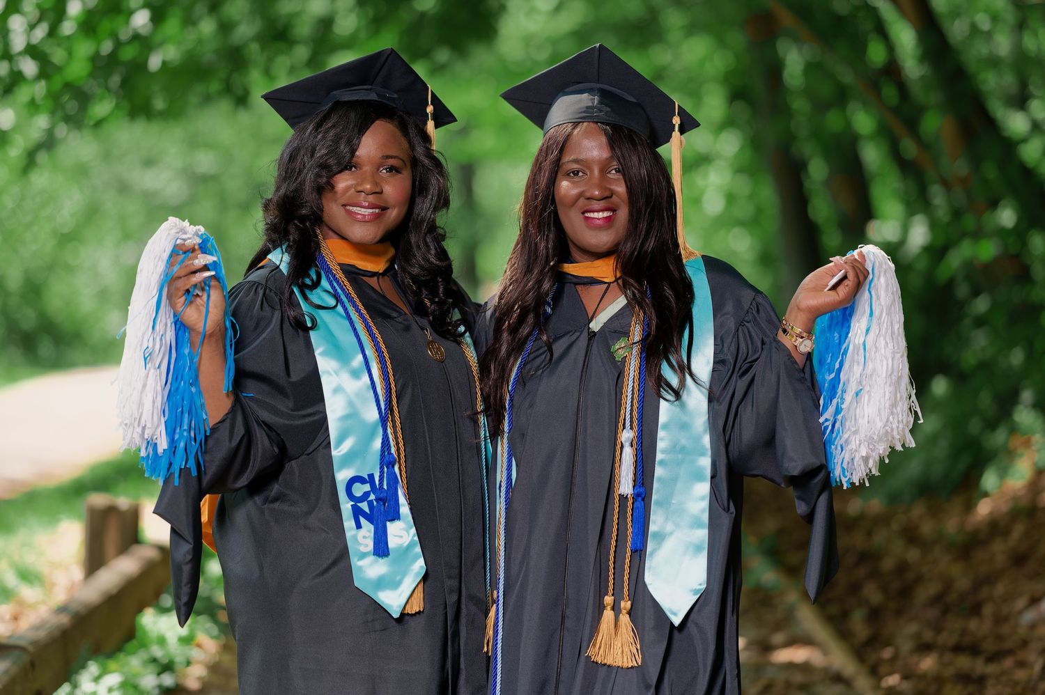 Group of graduates in black gowns holding blue tassels during celebration.