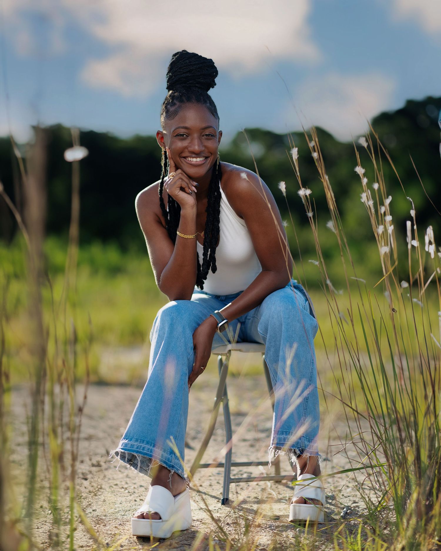 Candid outdoor portrait in denim and white top among tall grass at sunset.