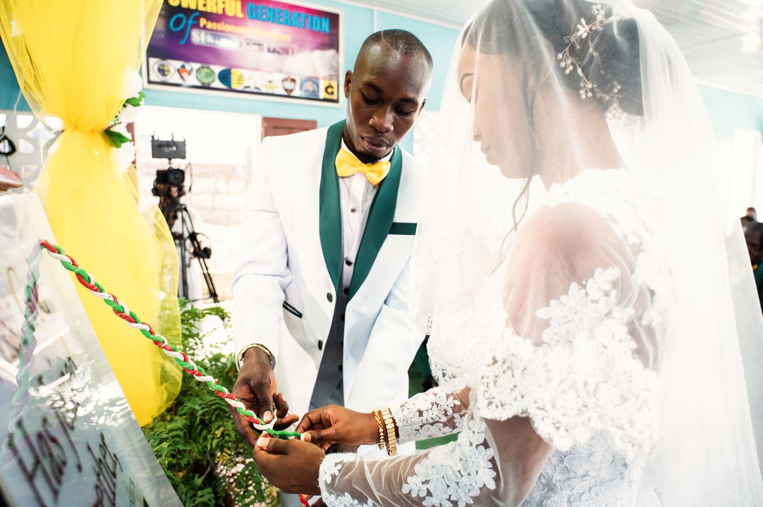 Bride and groom in elegant wedding attire signing documents at a decorated ceremony table with floral arrangements.