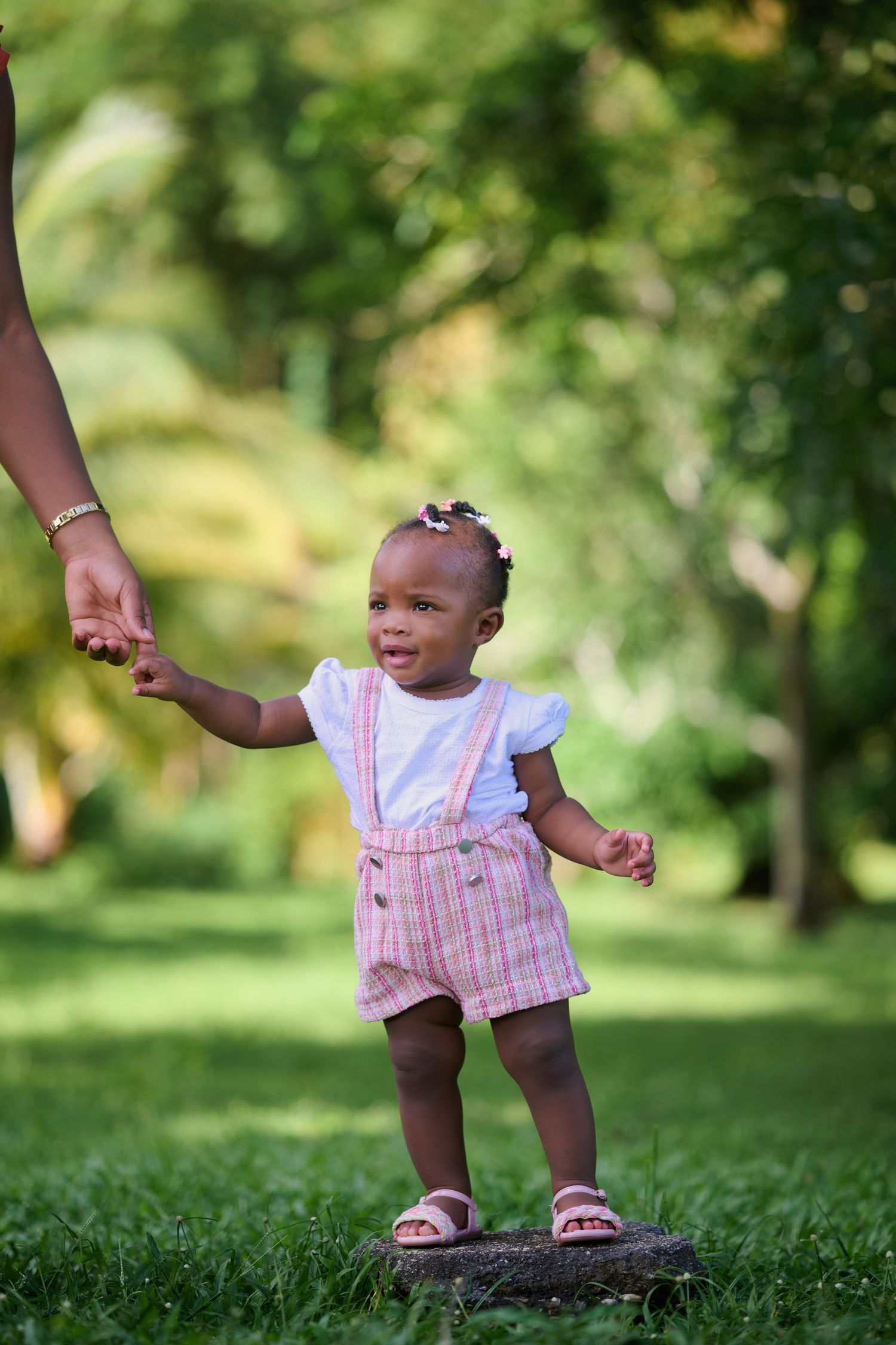 Small child in pink striped outfit taking first steps on grass.