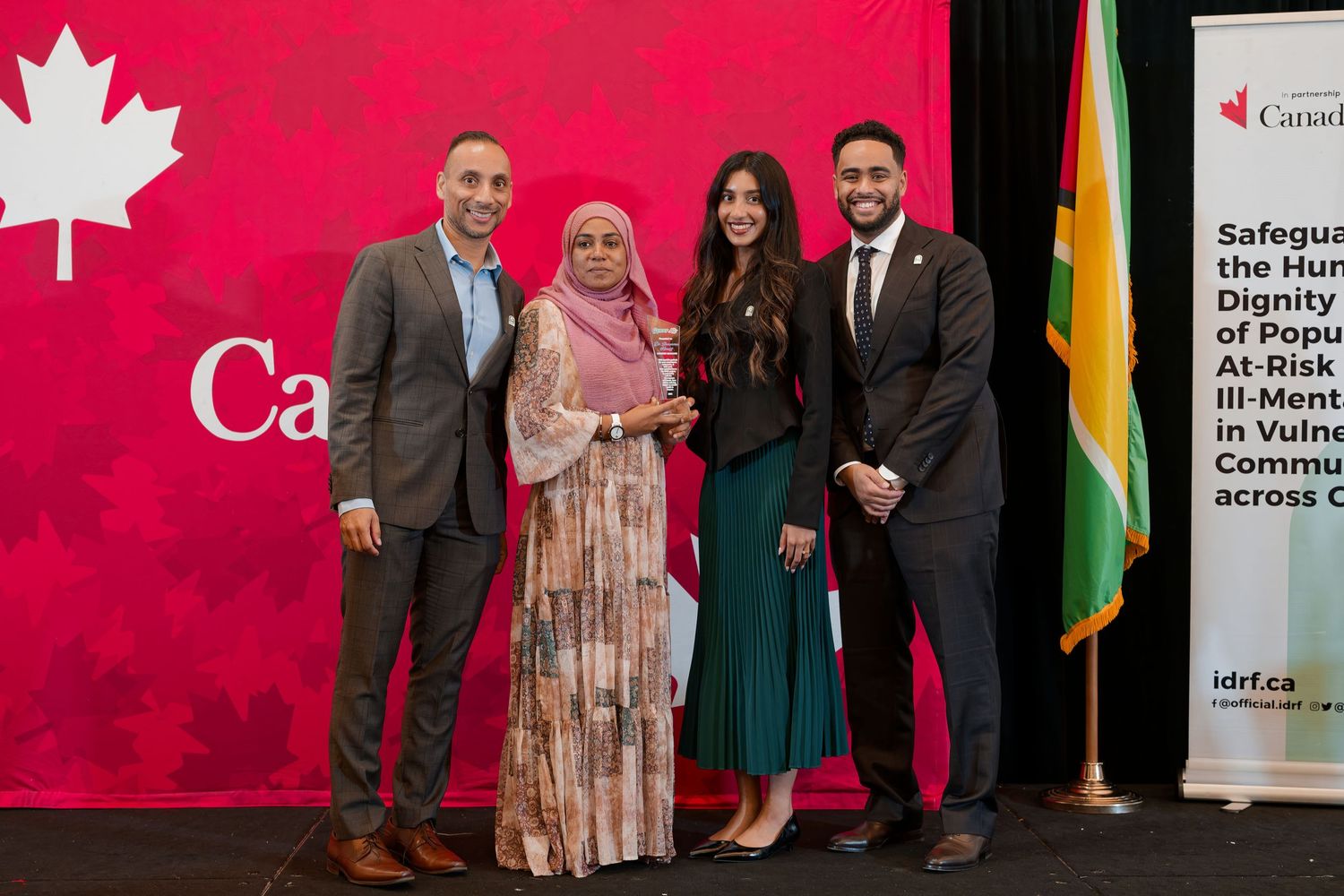 Four people pose for a photo at a Canadian government award ceremony with a red maple leaf backdrop.