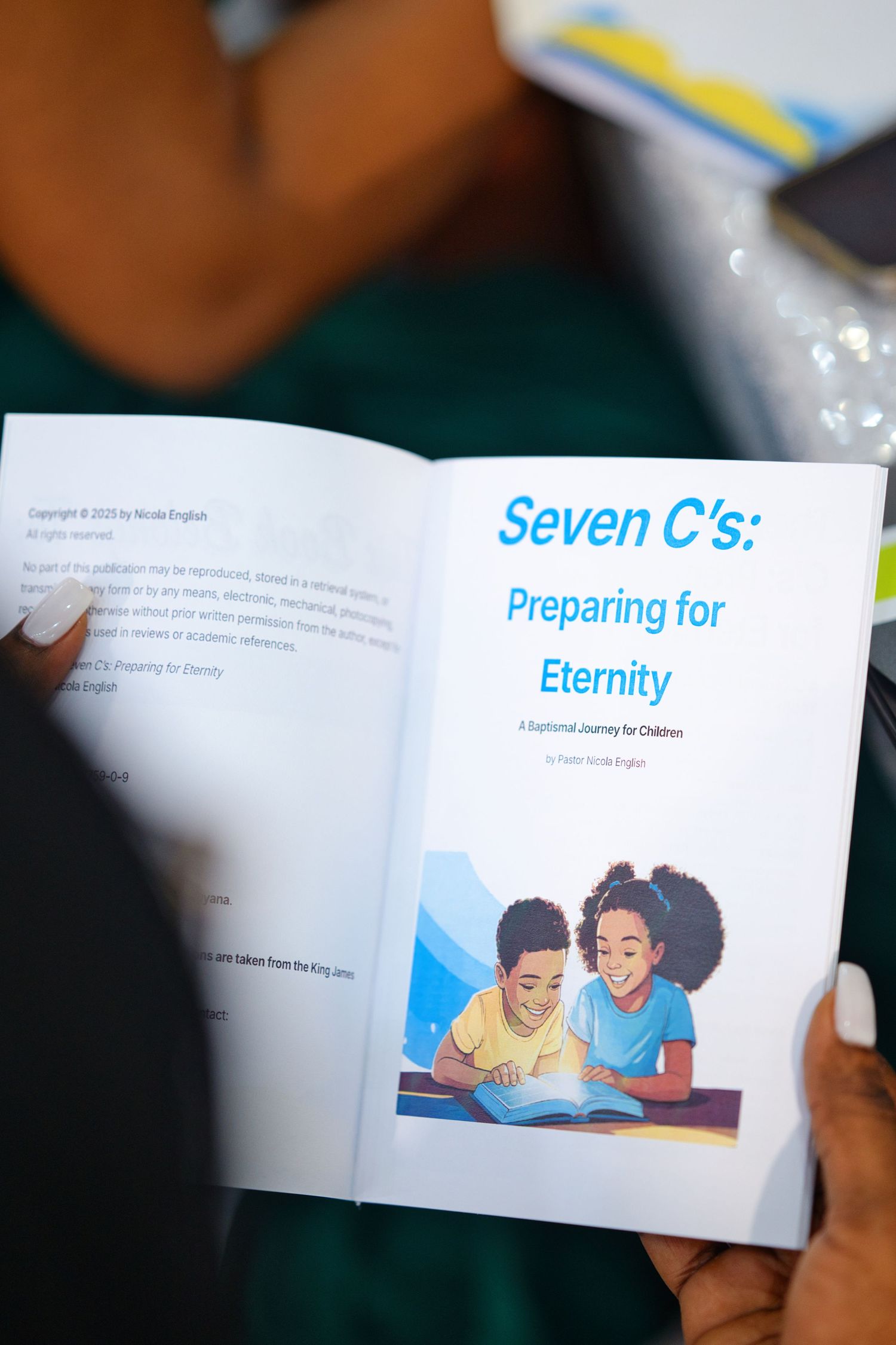 Hands holding open a children's spiritual book titled Seven C's: Preparing for Eternity by Pastor Nicole English.