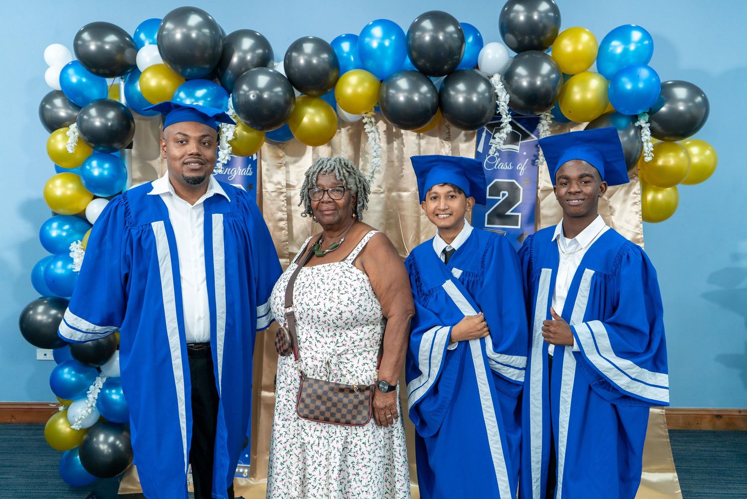 Graduation celebration with blue and gold balloon decorations and graduates in blue caps and gowns.
