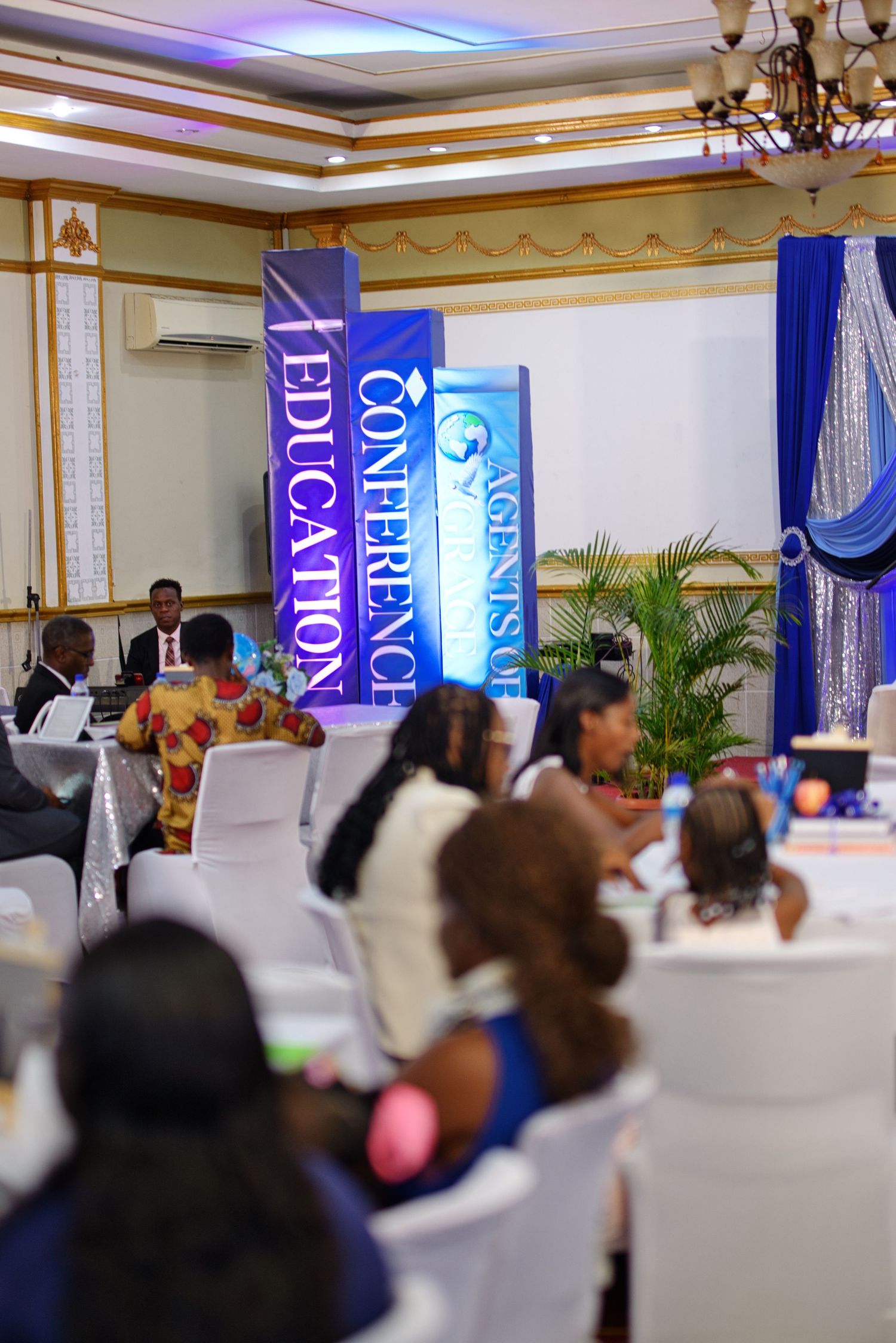 Agents of Change Education Conference attendees seated at banquet tables in an elegant hall with blue decorative banners.