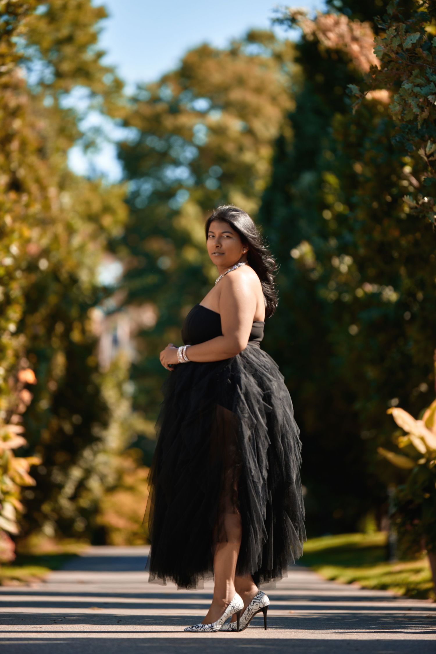 Fashion portrait featuring a black tulle dress on a sunlit outdoor pathway.