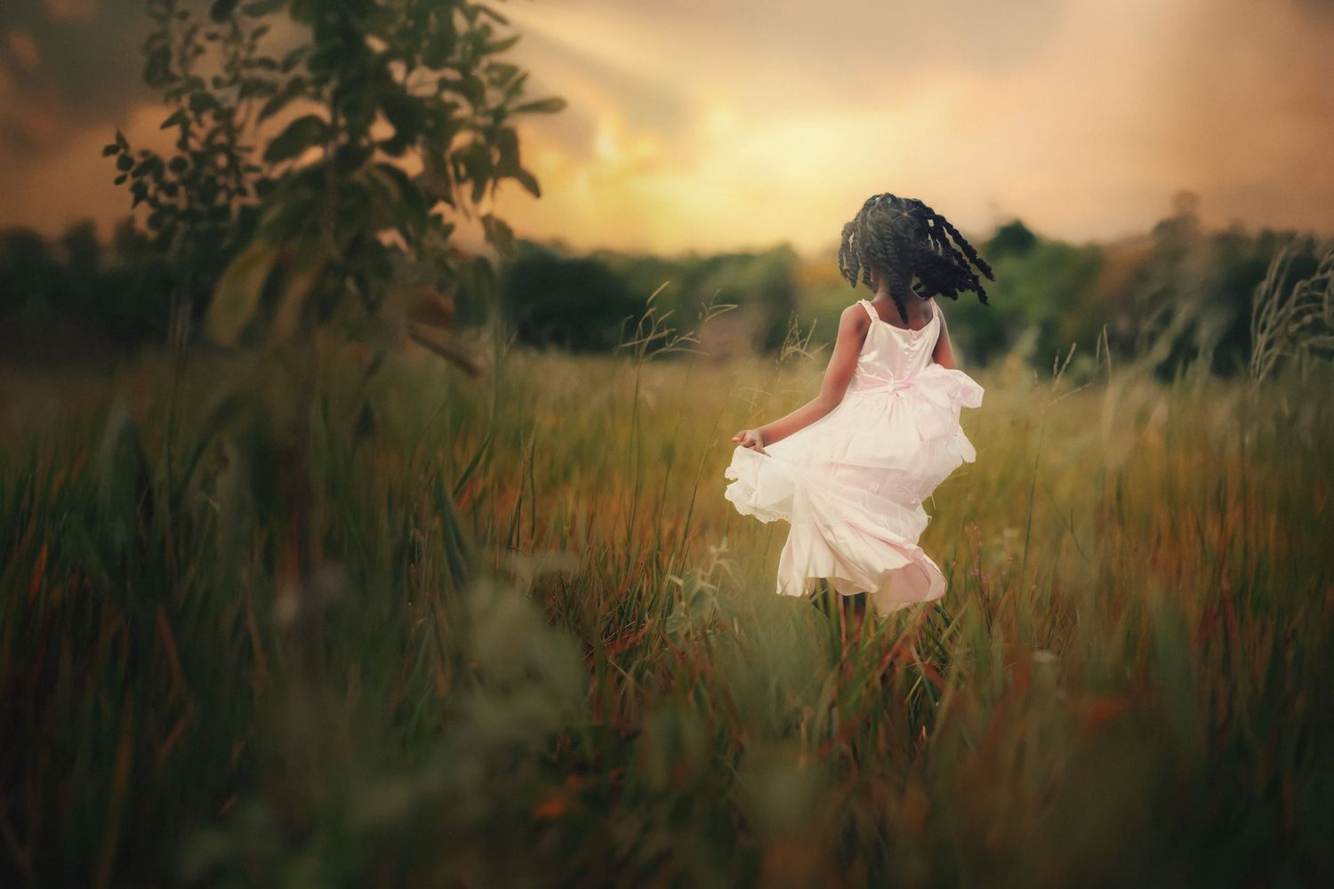 Child in white dress twirls in golden field at sunset.