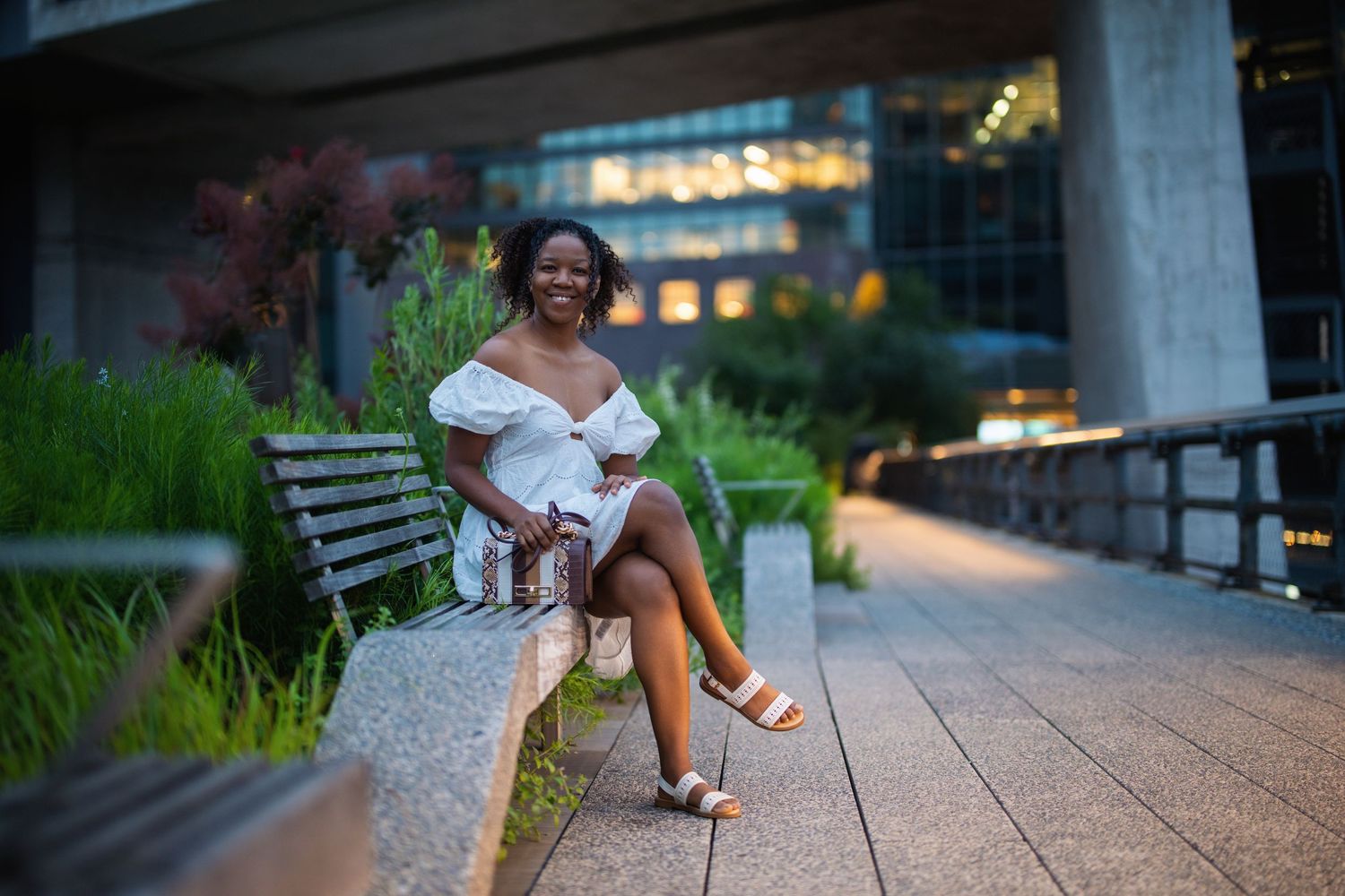 Person in white dress sits elegantly on urban walkway at twilight.