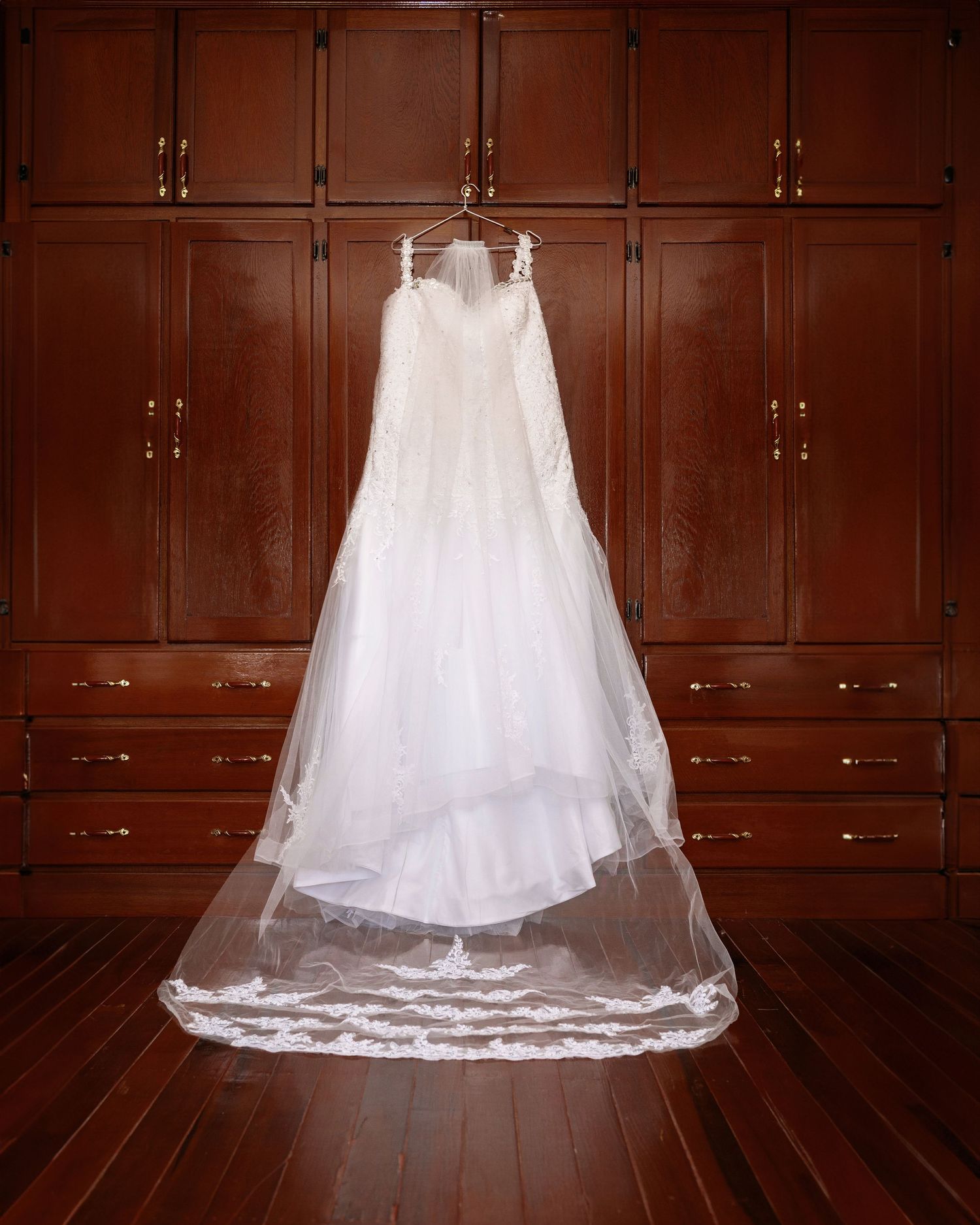 An elegant white wedding dress hangs gracefully against dark wooden cabinets.