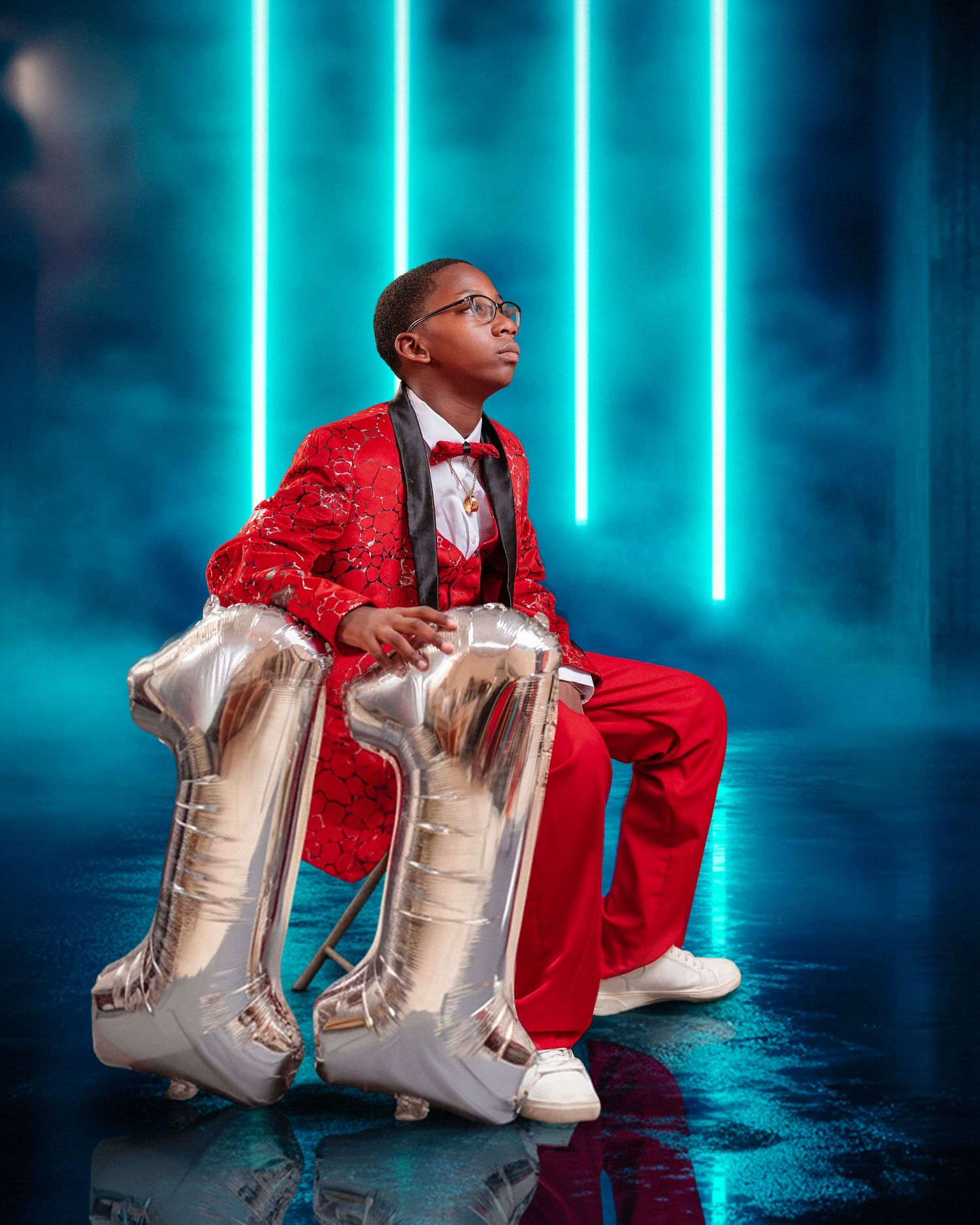 A young performer in a red jacket and glasses poses dramatically against a blue backdrop with neon lights.