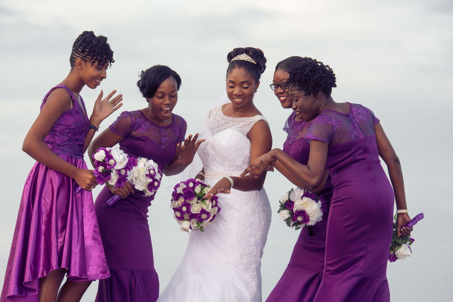 Bridesmaids in purple dresses share a joyful moment with the bride on the beach.