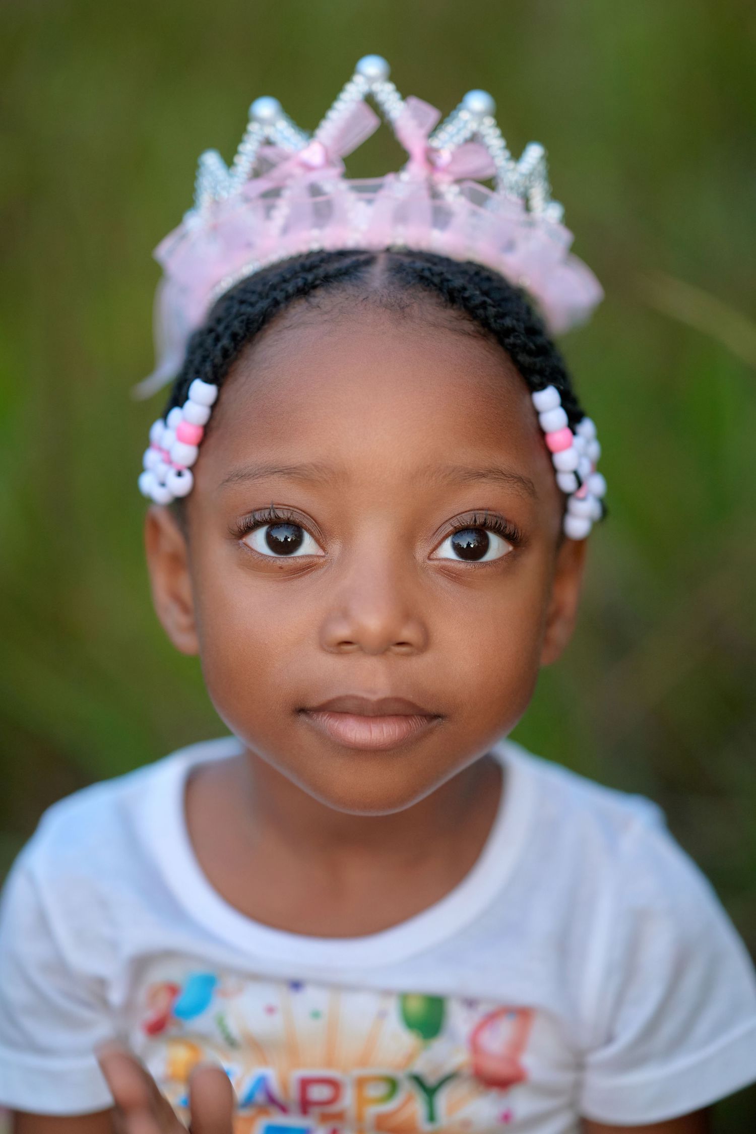 Child wearing white t-shirt and floral accessories against natural green background.