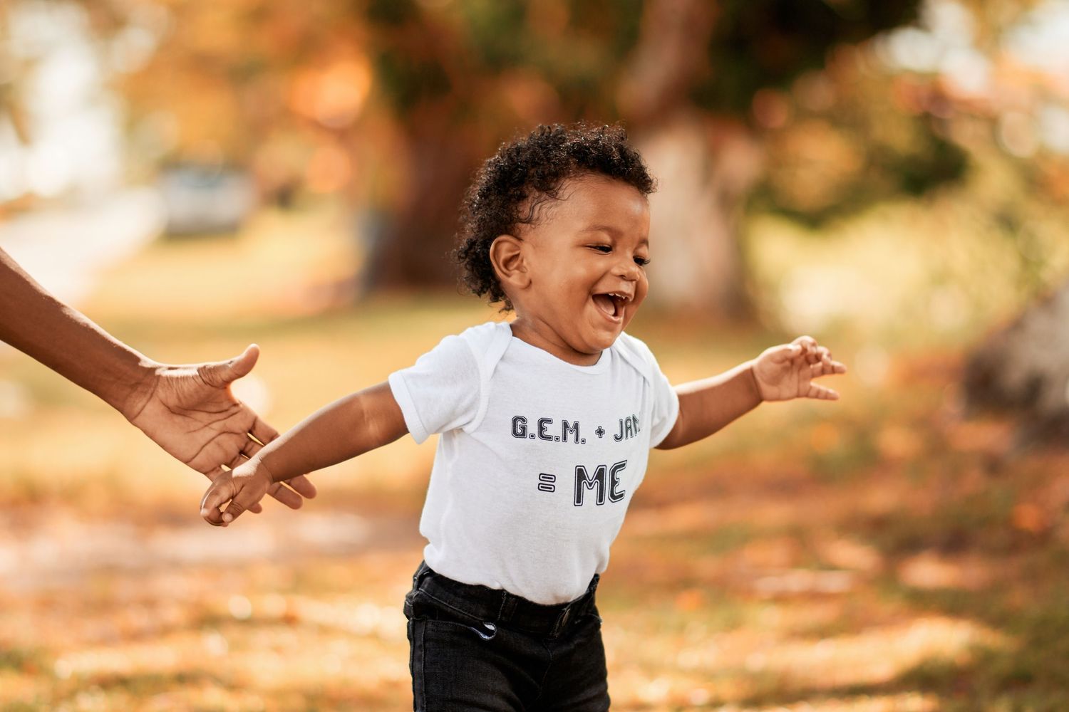 Child in white t-shirt playing joyfully in autumn sunlight.