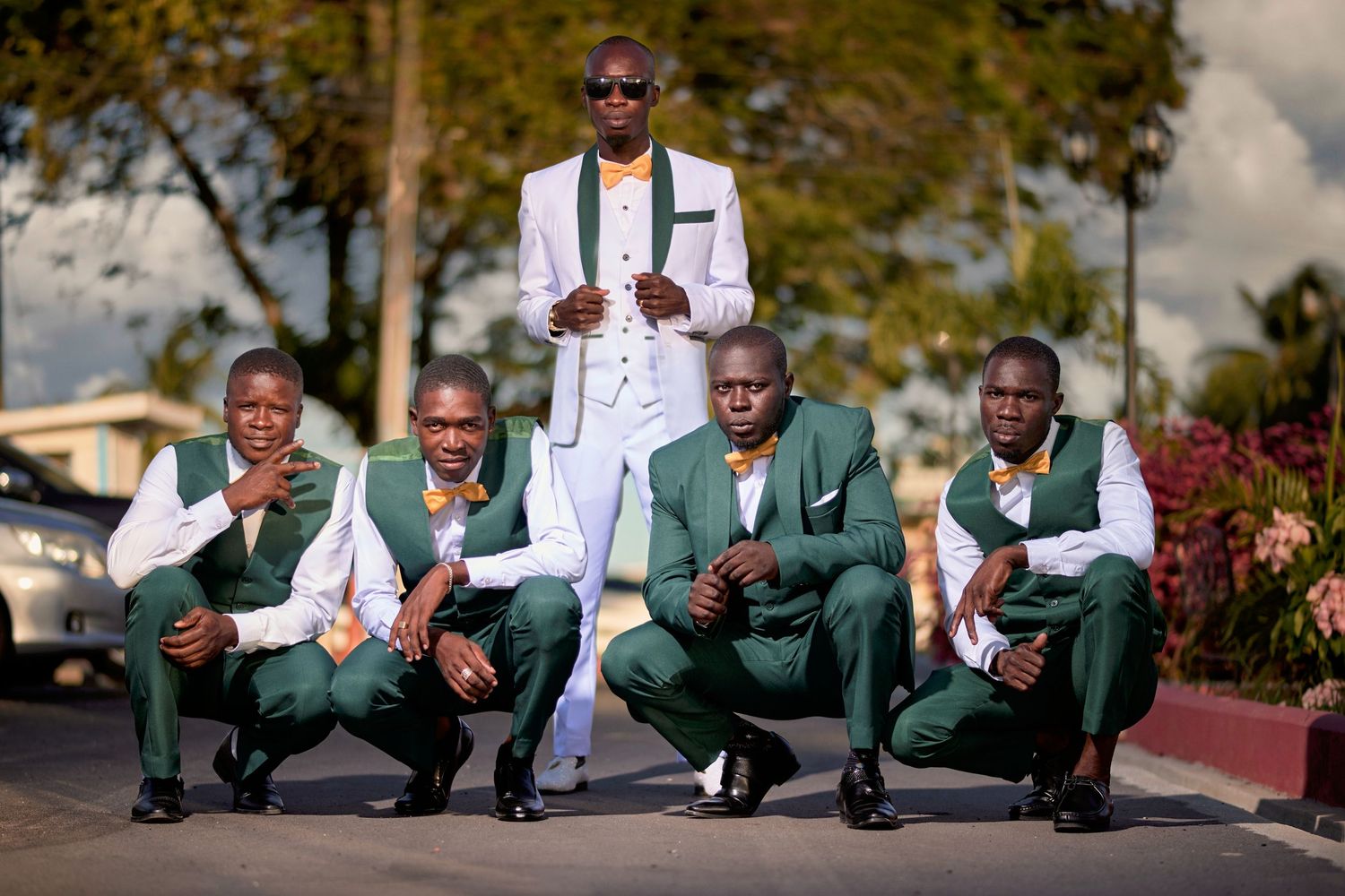 Groomsmen in green vests and white jackets pose in stylish formation on sunny day.