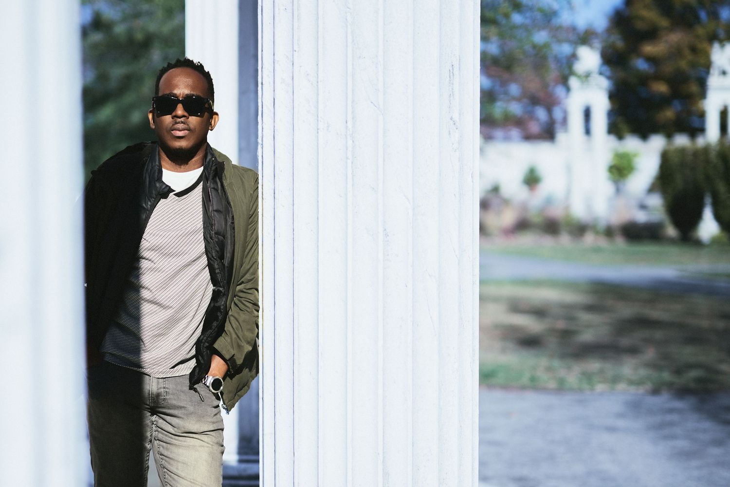 Person in casual attire poses against white columns in outdoor setting.