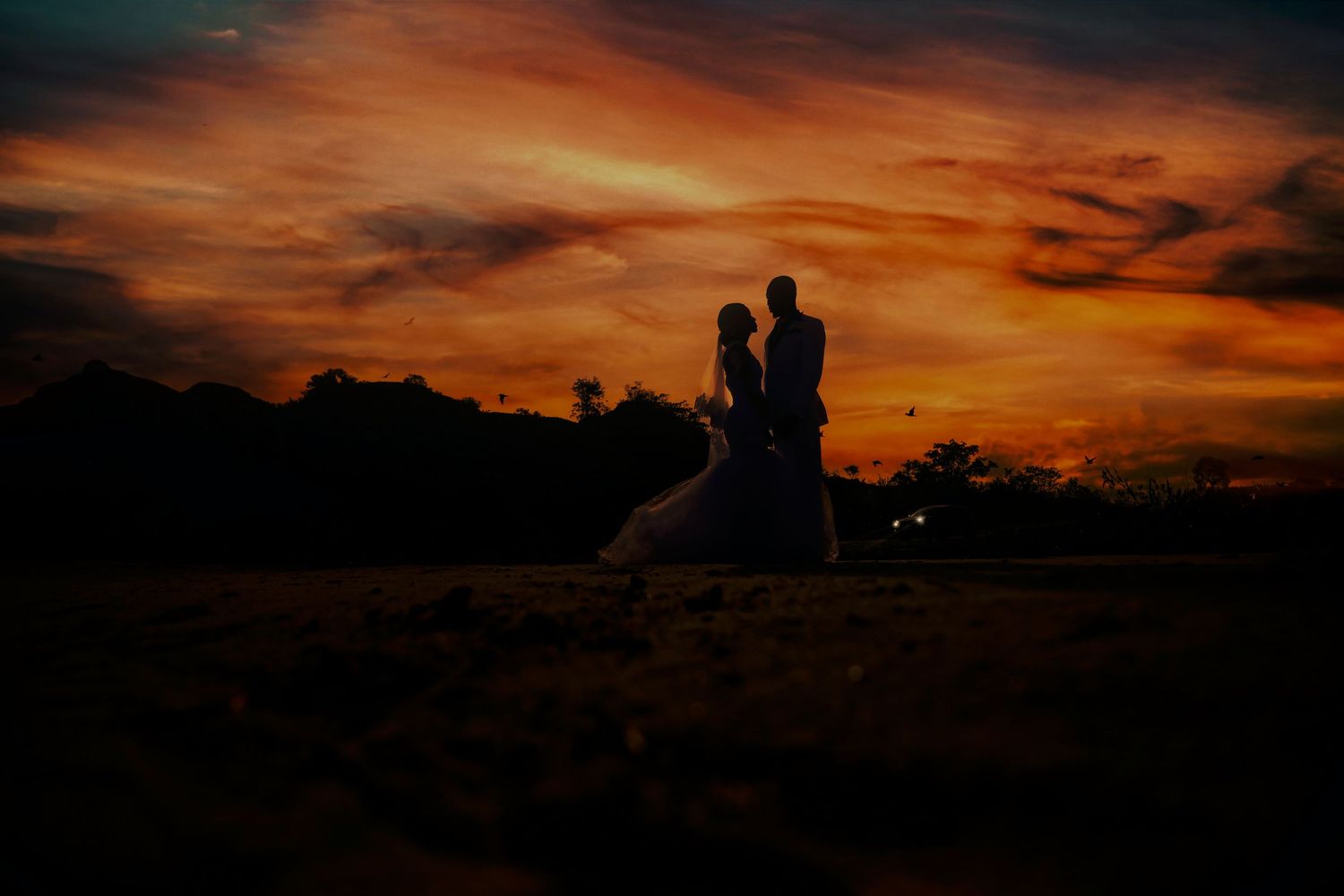Silhouette of newlyweds against a dramatic orange and red sunset sky.