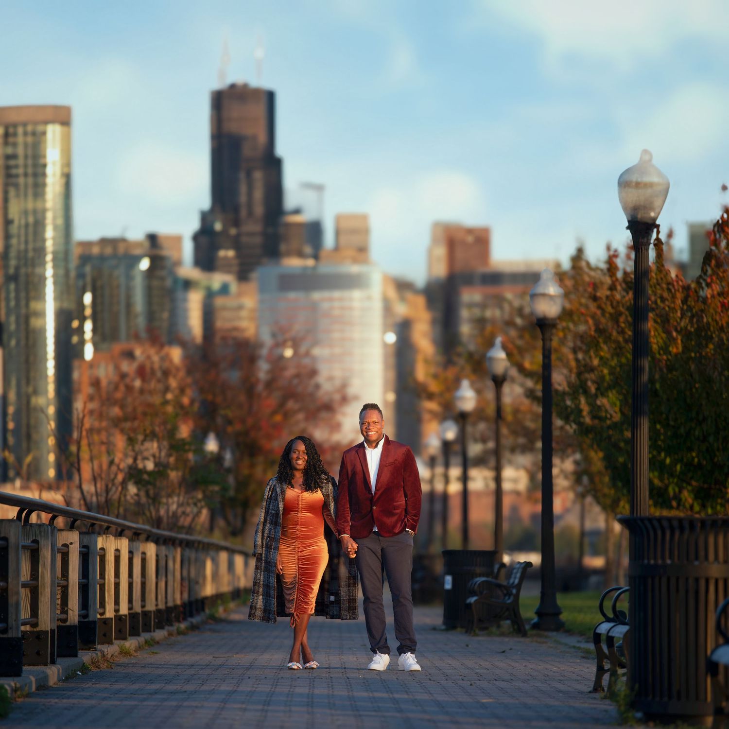 A couple walks along a path with the Manhattan skyline visible in the distance.