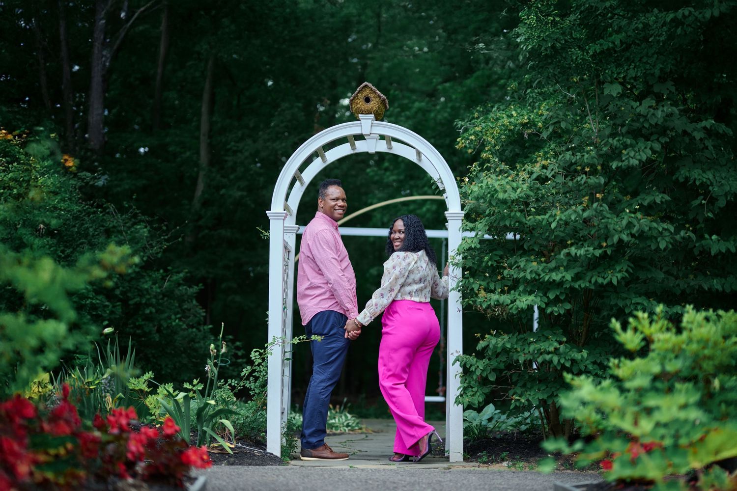 White garden arch frames a romantic outdoor scene in a wooded area.