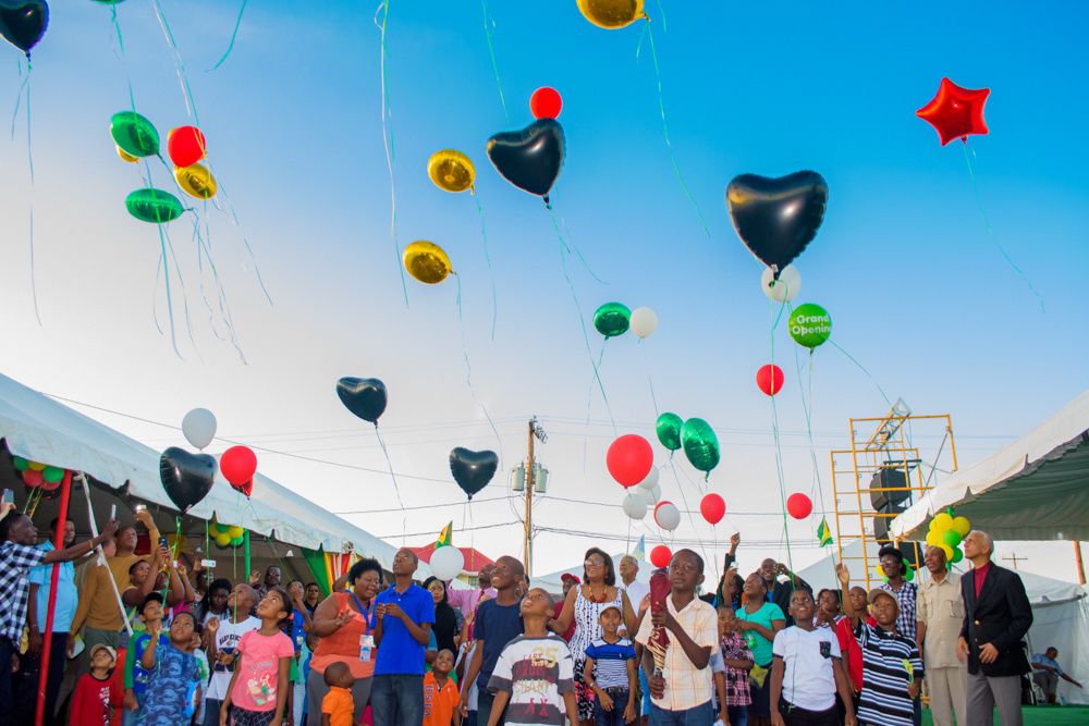 Crowd releasing colorful balloons into bright blue sky during outdoor celebration.