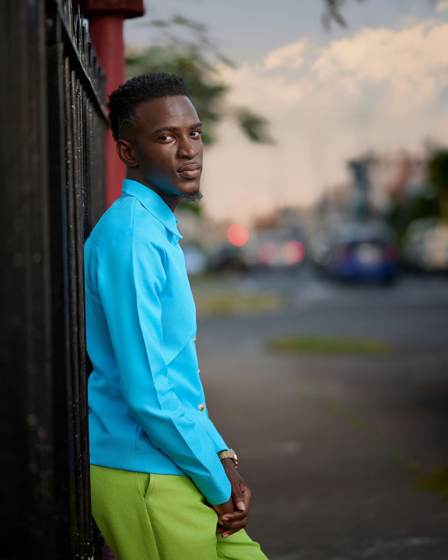 Evening portrait in bright blue shirt and lime green pants against urban backdrop.