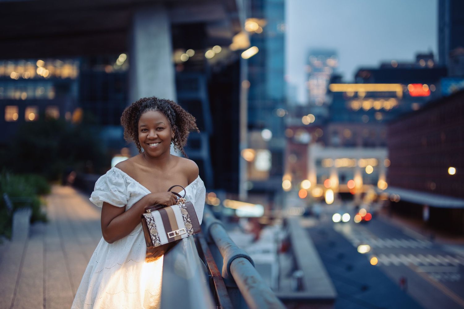 Person in white dress poses with balloons on urban rooftop at dusk.