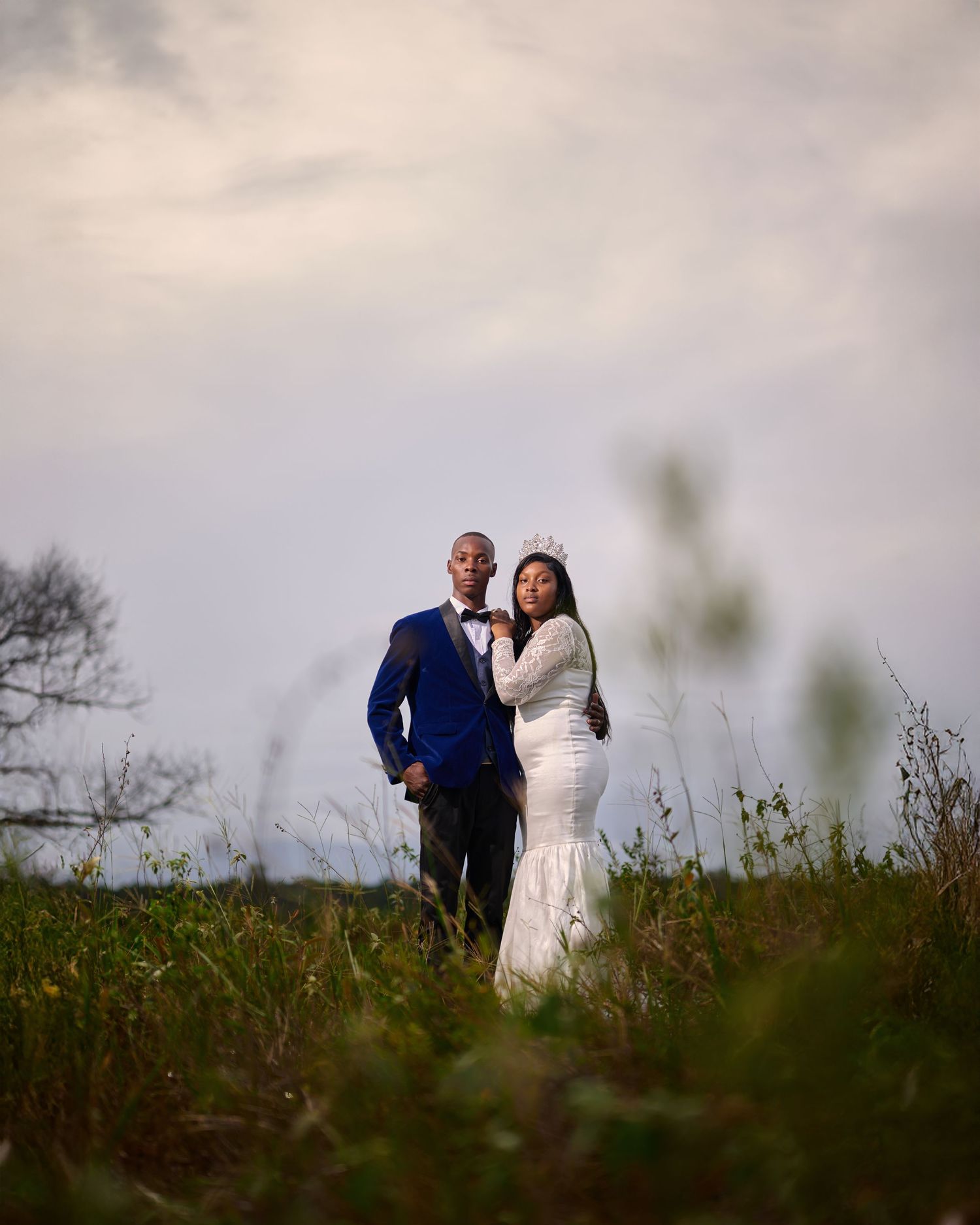 Couple poses together on a hilltop against a cloudy sky during their wedding photoshoot.