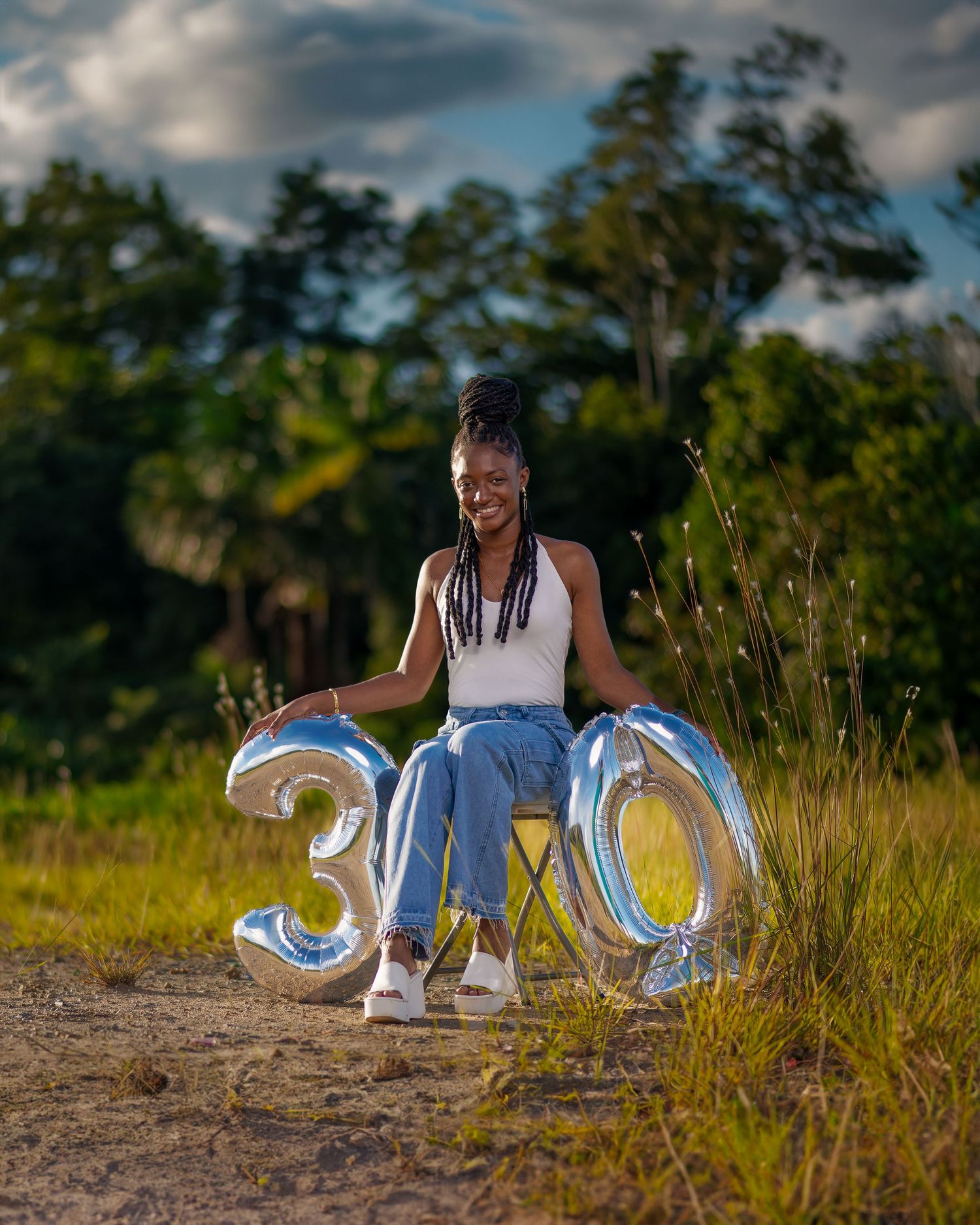 A creative graduation photo shoot in a grassy field with illuminated 2023 numbers at sunset.