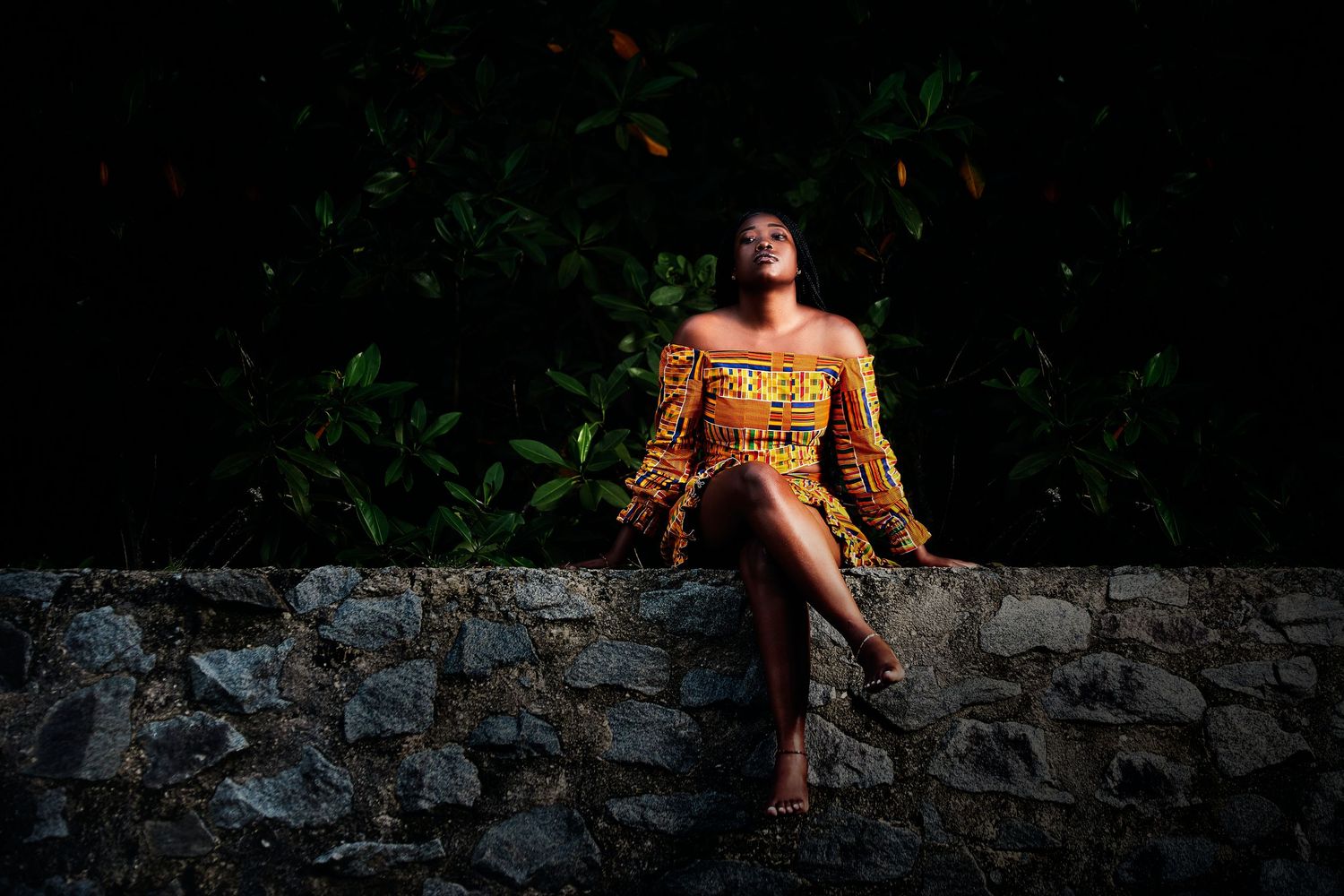 Artistic portrait against stone wall backdrop with dramatic lighting and traditional attire.