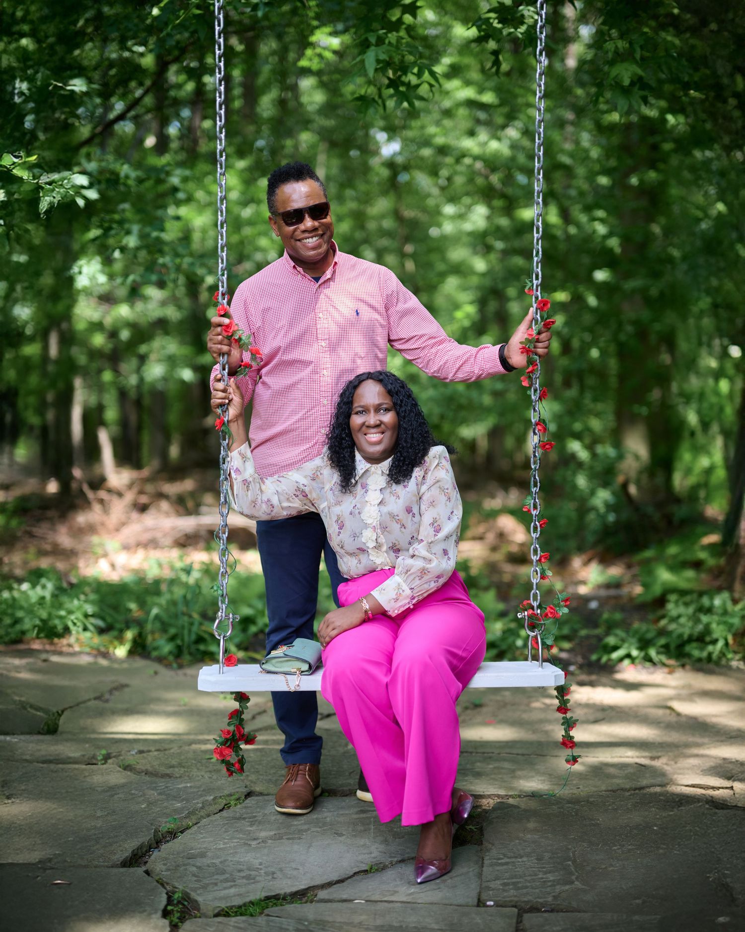 Couple enjoying a playful moment on a swing in a wooded park setting.
