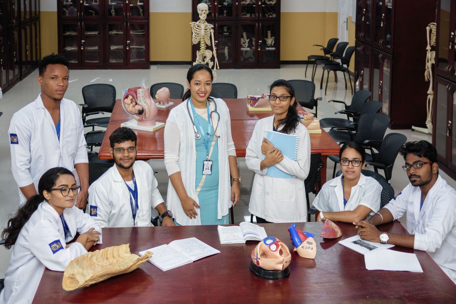 Medical students in white coats gathered around a table during a laboratory session.