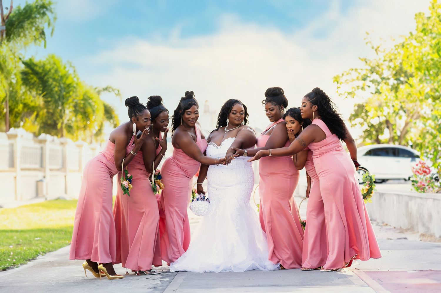 Bridesmaids in pink dresses pose together outdoors on a sunny day.