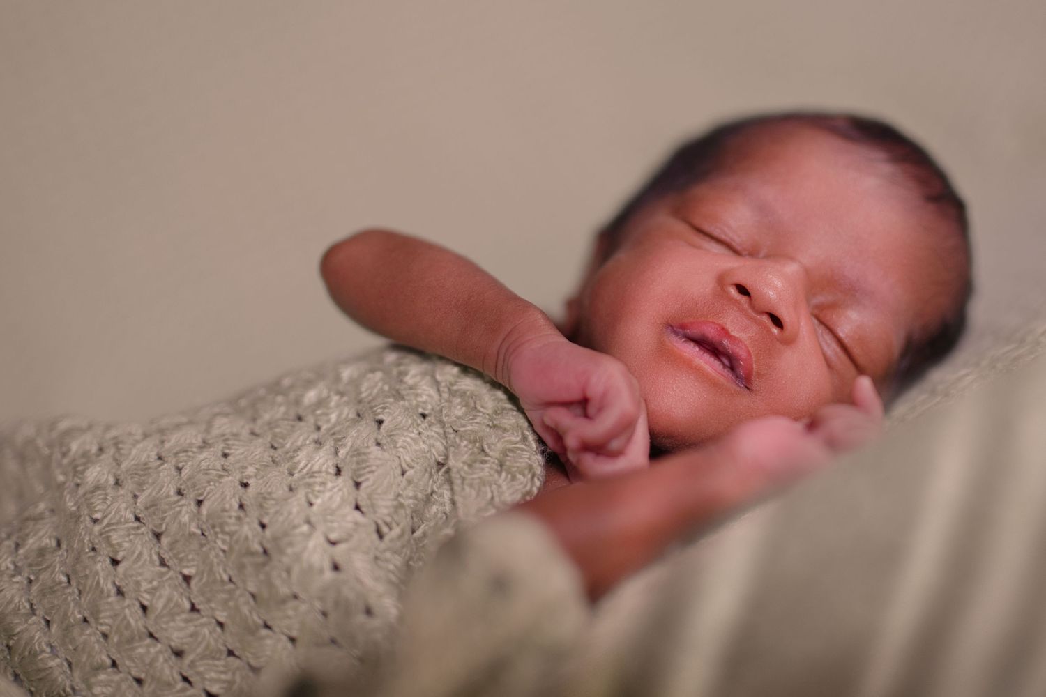 Newborn baby sleeping peacefully on soft white blanket in gentle lighting.