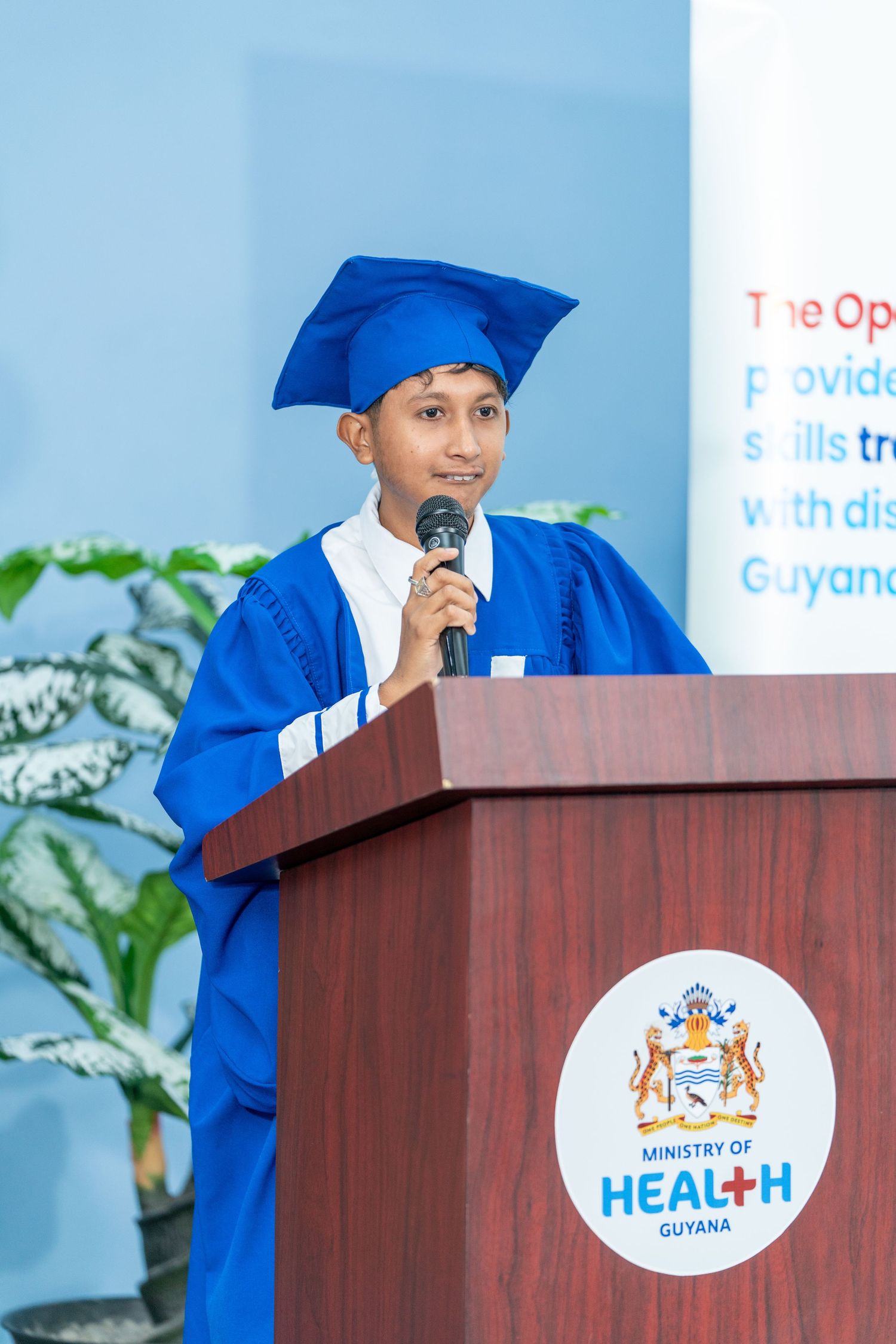 Graduate speaking at podium with Health Ministry logo during ceremony.