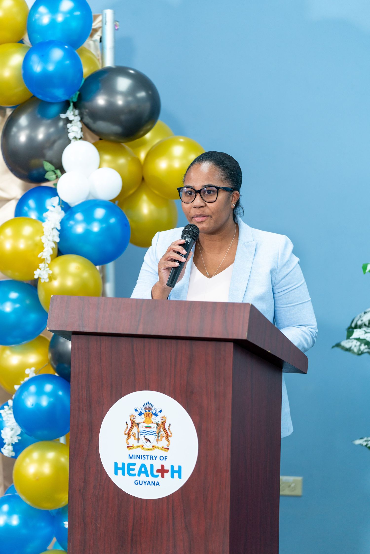 Conference speaker at podium with blue and gold balloon decorations and health organization logo.