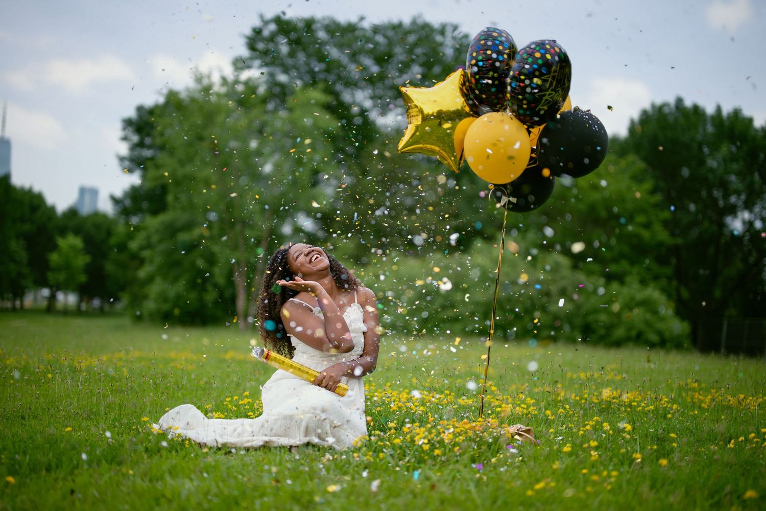 Festive outdoor photoshoot with colorful balloons and confetti in a sunny park setting.
