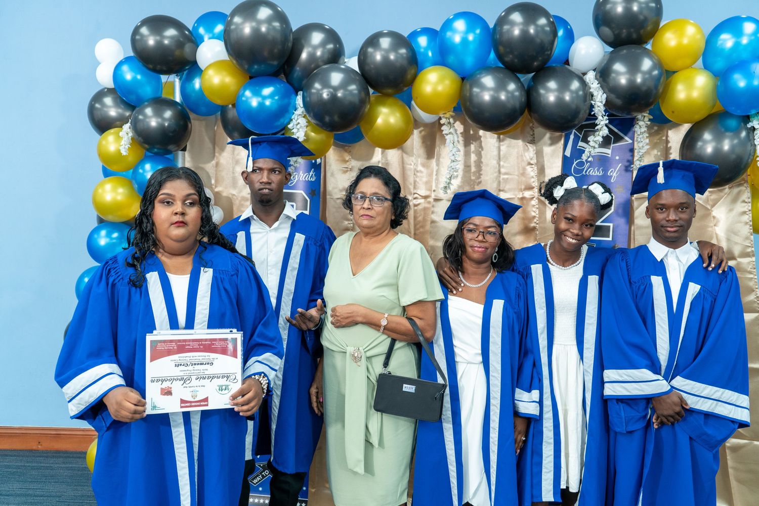 Group photo of graduates in blue regalia with festive balloon arch backdrop.