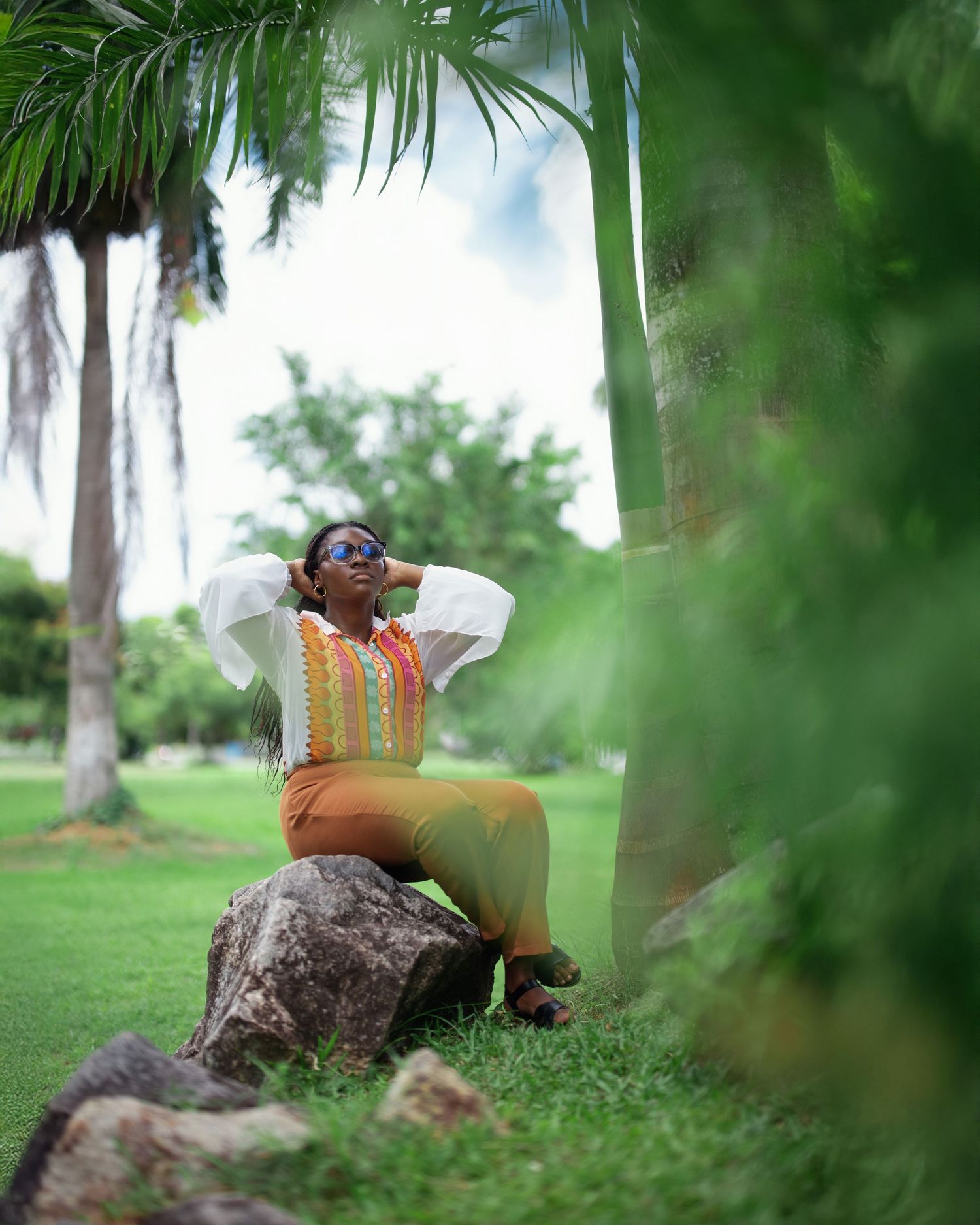 Artistic outdoor photoshoot among palm trees and greenery with white and orange outfit.