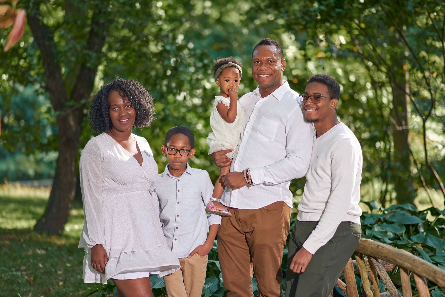 Family wearing coordinated white outfits poses together outdoors in a park setting.
